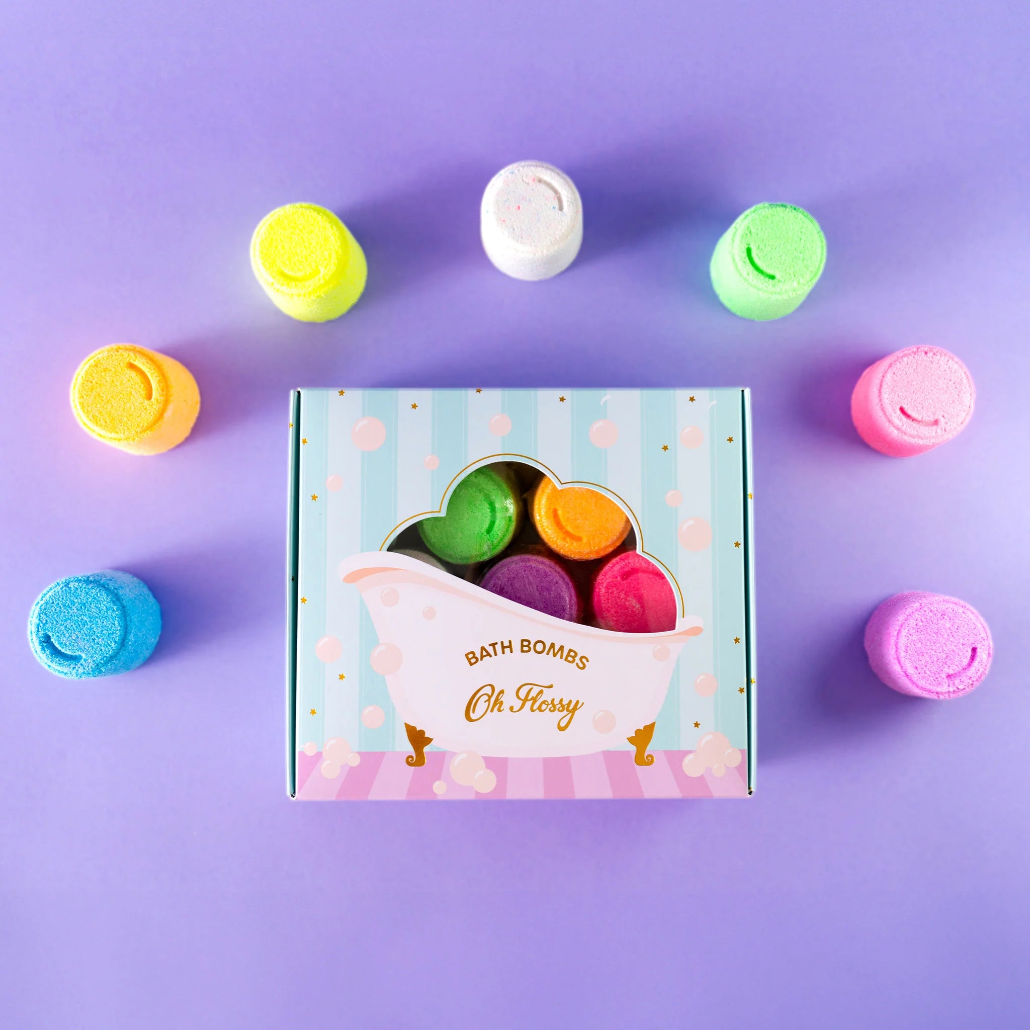 The Oh Flossy Kids Mini Bath Bombs set sits on a purple background. An open "Oh Flossy" box reveals multicolored bath bombs, gentle on kids' skin, arranged in a circle. The packaging has a cute bathtub design and is handmade in Australia.