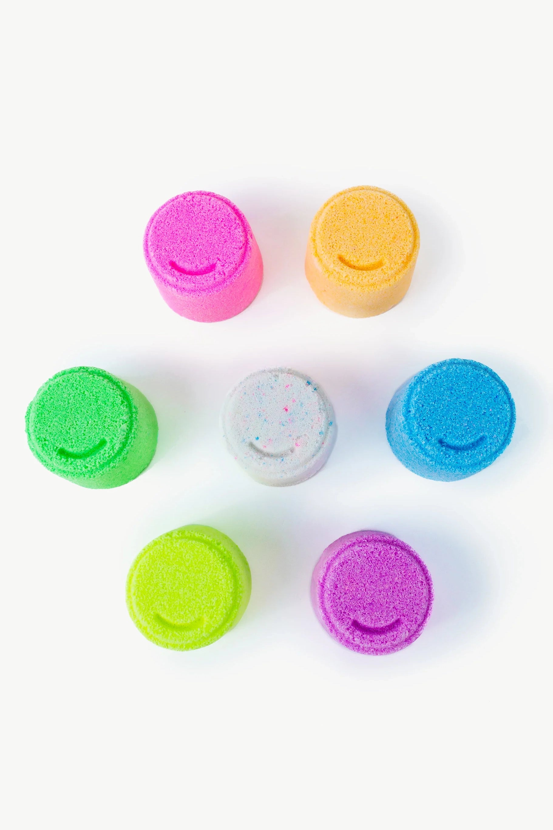 Seven handmade Oh Flossy bath bomb cylinders, crafted in Australia, are arranged on a white surface. The colors—pink, orange, blue, purple, green, mint, and yellow—stand upright and distinct. This visually pleasing pattern is gentle on kids' skin with its soft pastel shades from OH FLOSSY.