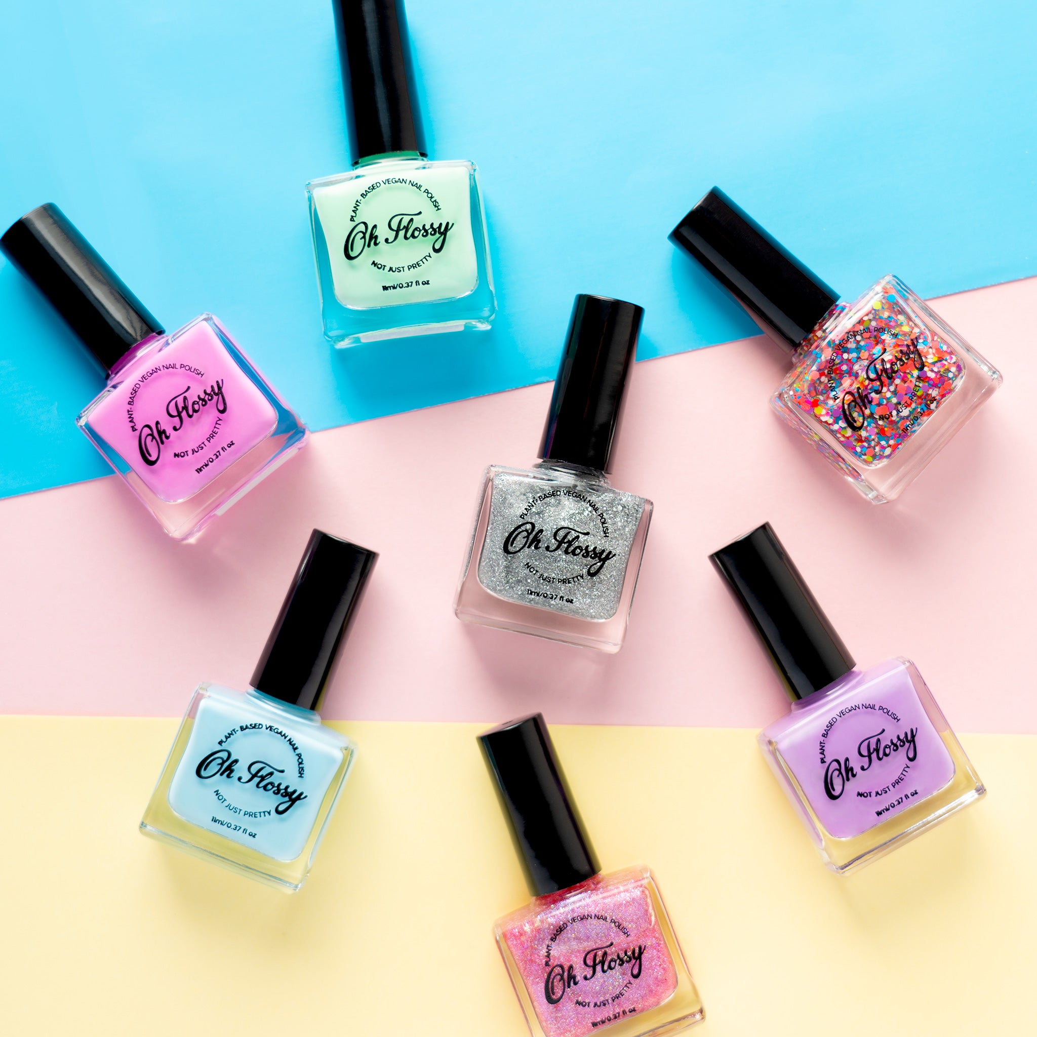 Seven bottles of Oh Flossy nail polish, including pink, teal, silver, glitter, and more, are displayed on a pastel background. Each bottle has a black cap and the "Oh Flossy" label. This plant-based collection is 10-free for safer use.