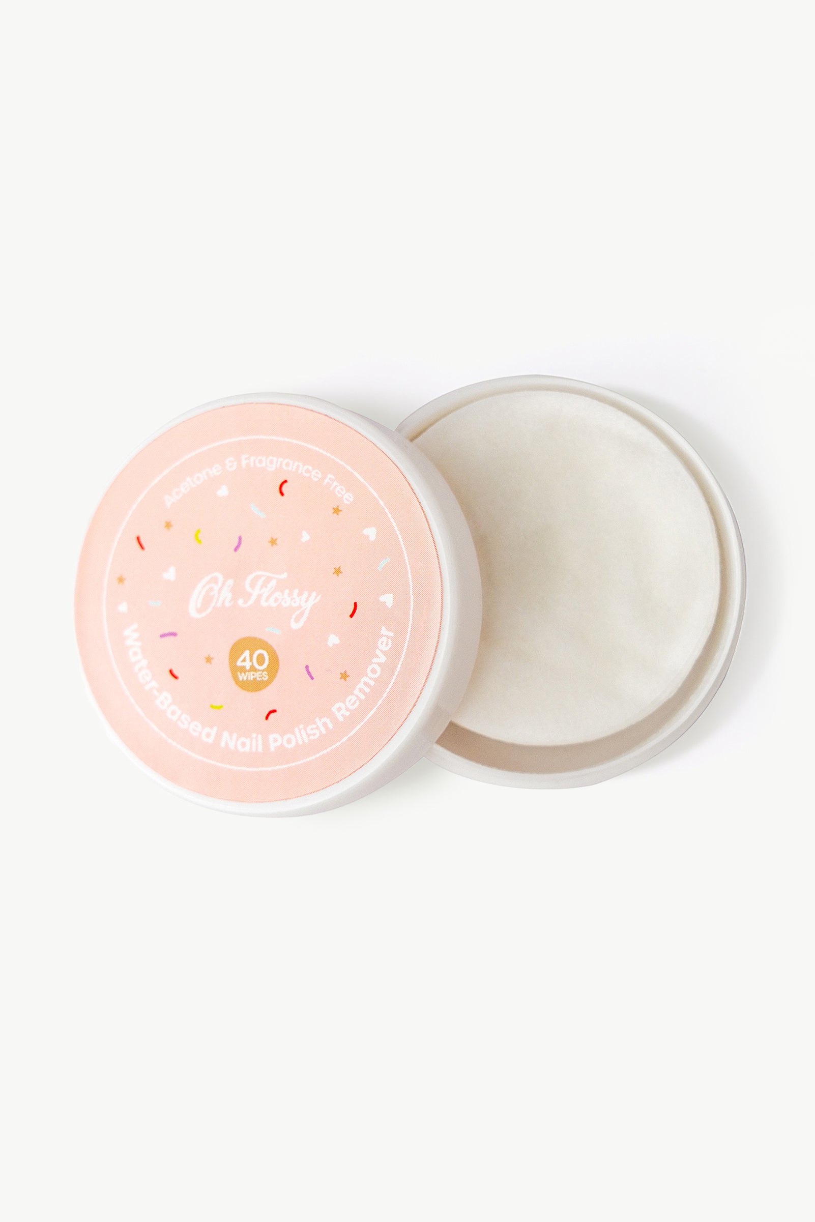 An open, round container with a pink lid, labeled "Oh Flossy - Water-Based Nail Polish Remover Wipes" by OH FLOSSY, reveals white wipes inside. The label notes its vegan formula and that it’s acetone- and fragrance-free.