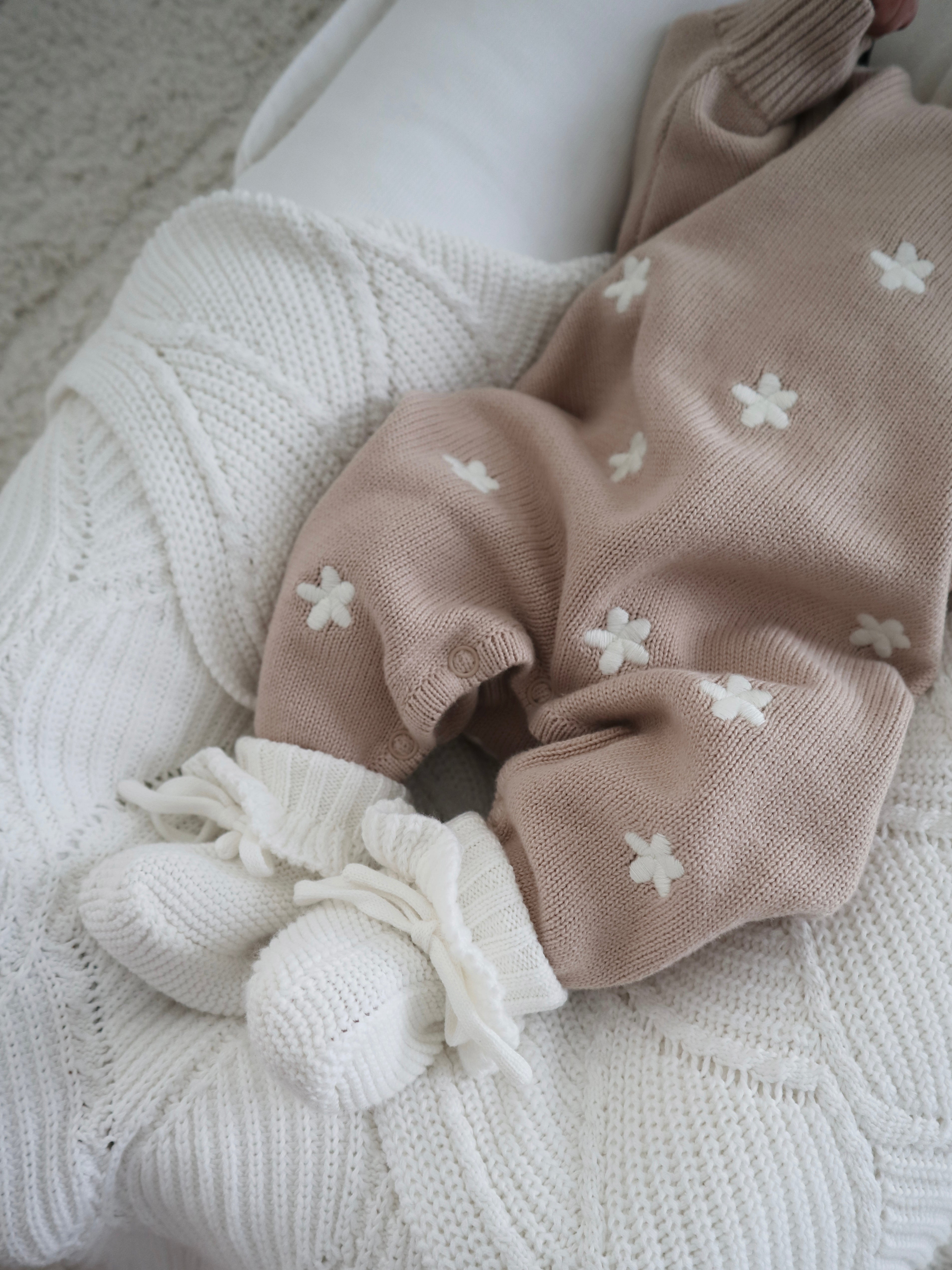 A baby wearing the ZIGGY LOU Winter Playsuit Aurora in size NB is lying on a white textured knit blanket.
