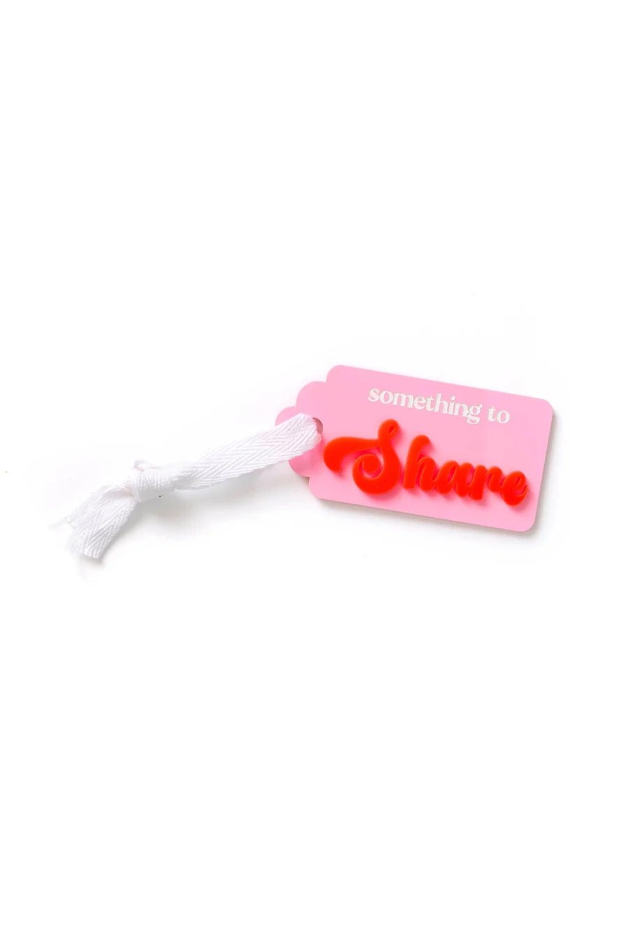 The HELLO KIT CO "Something to SHARE Tag Pink/Red" features a pink acrylic design with a white ribbon, showcasing the phrase "something to Share" in striking red and white letters, embodying the essence of meaningful gifting.