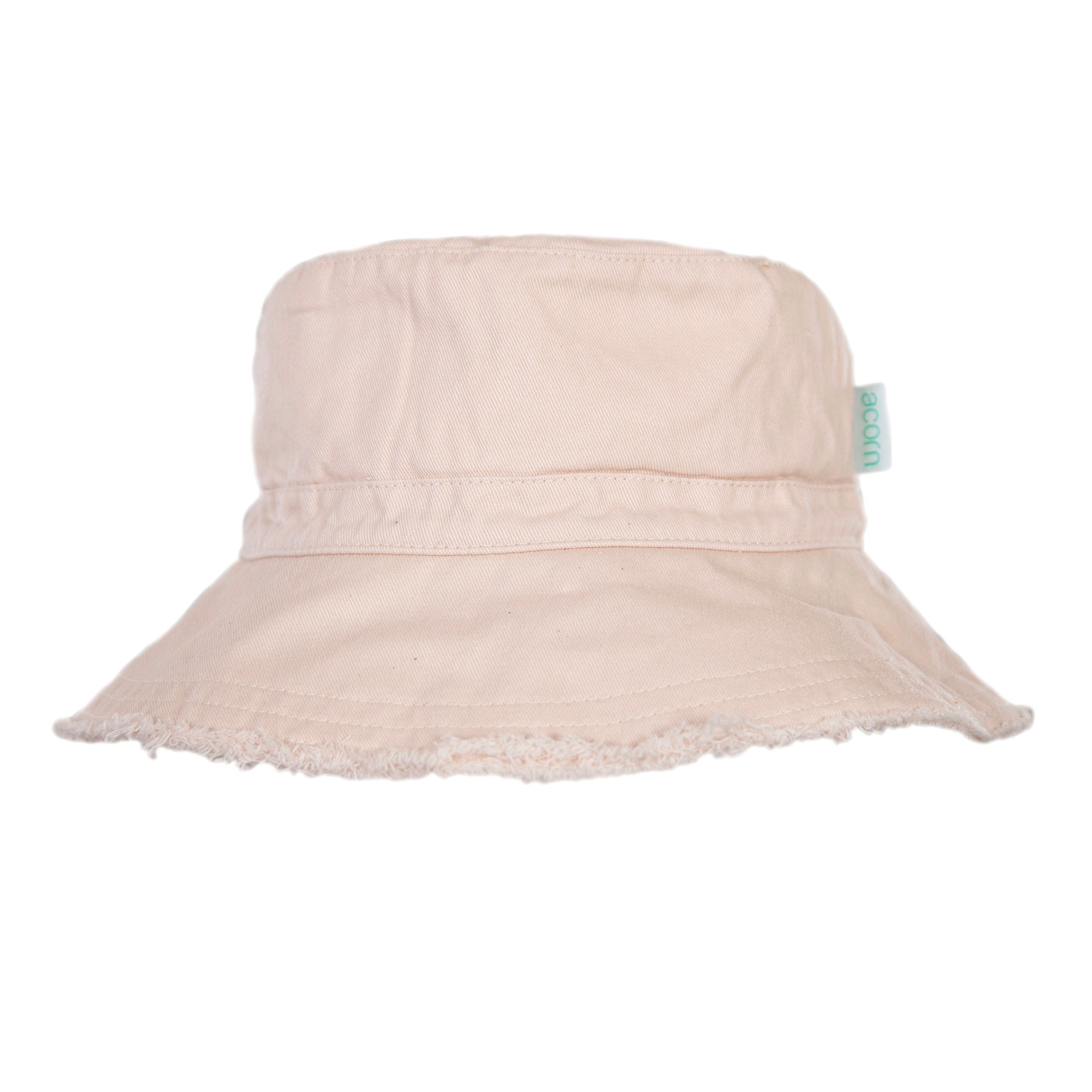 The Frayed Bucket Hat Vanilla by ACORN KIDS is a vanilla-colored bucket hat featuring a slightly frayed brim and a cloth tag with a blue logo on the side. Made from soft, lightweight cotton twill, it also offers UPF50+ sun protection. The background is plain and white.