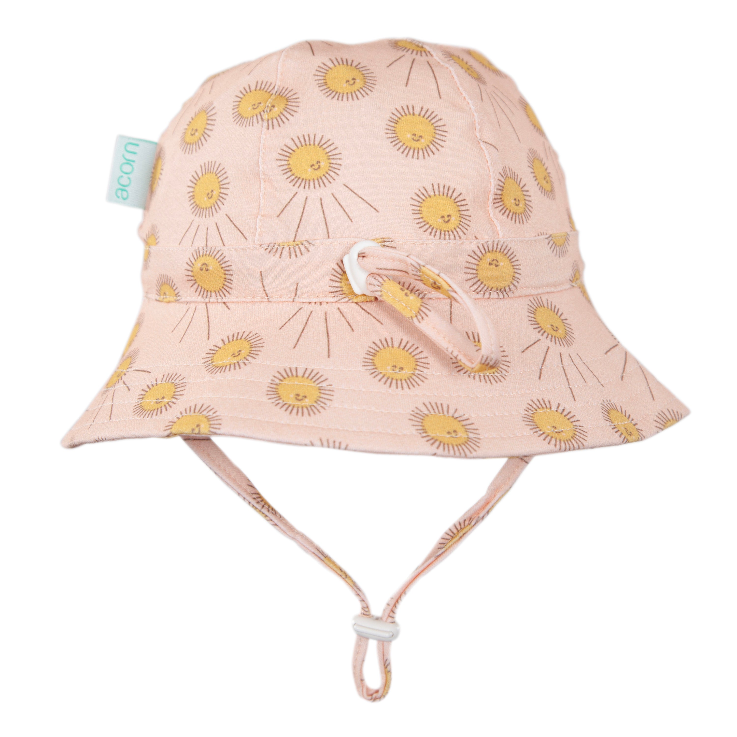 The Acorn Kids - Sunshine Stretch Cotton Wide Brim Sunhat by ACORN KIDS features light pink stretch cotton, a yellow sun pattern, UPF50+ protection, chin straps, and a small green "acorn" tag on the side.
