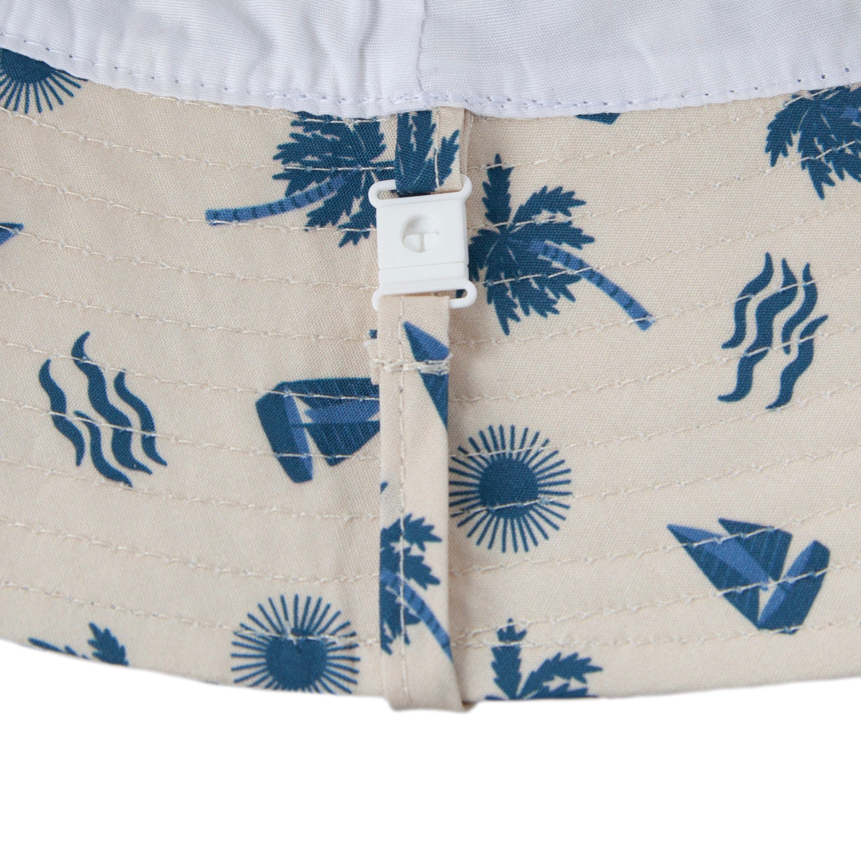 Close-up of the Acorn Kids - Island Breeze Wide Brim Bucket Hat by ACORN KIDS: a beige cotton hat with blue tropical prints, white plastic toggle, and drawstring. Features UPF50+ sun protection for outdoor adventures.