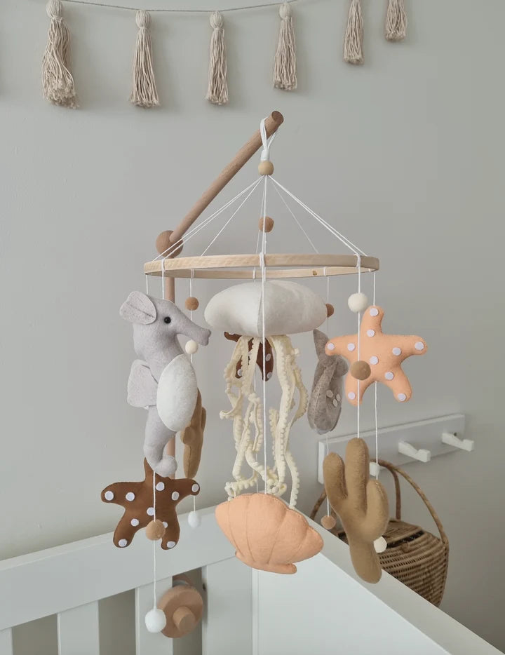 The ROOMI & ME Roomi & Me - Baby Mobile Underwater Dreaming is a handmade, neutral-toned nursery decor featuring plush sea creatures, a mouse, starfish, jellyfish, seashells, and a hanging garland for gentle visual stimulation over any crib.