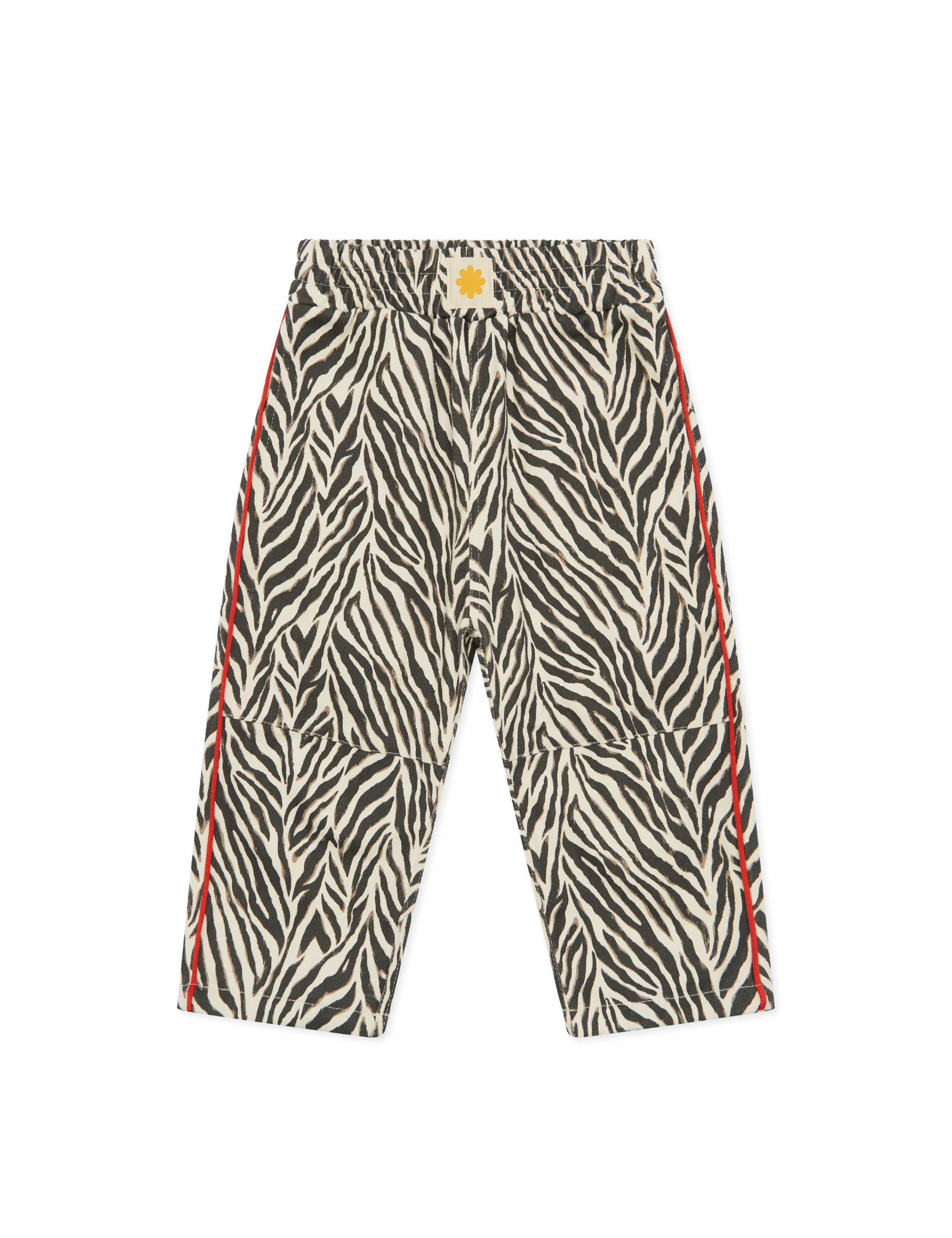 The SONNY LABEL Sonny Label - Animal Twill Pants Zebra features wide-legged cotton twill with a black and white zebra print, red side stripes, and a yellow flower emblem on the waistband, shown against a plain black background.