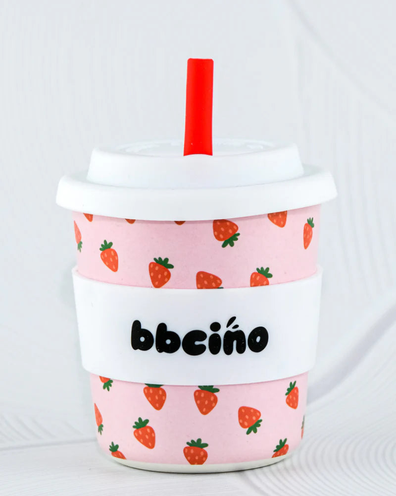 The BBcino Reusable BambinoCino Cup 240ml Berry BB by BBCINO is a pink cup with strawberry prints, a white lid, red straw, and white "bbcino" band—an eco-friendly option made from sustainably sourced bamboo.