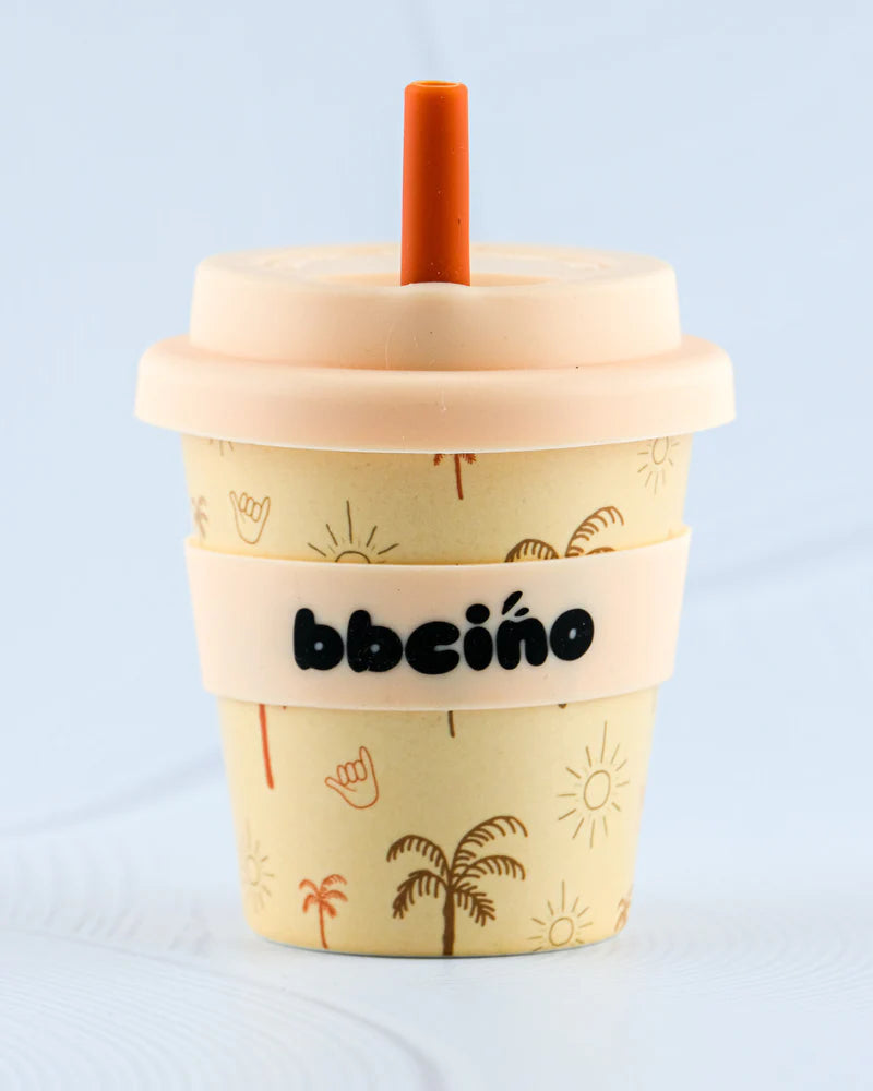 The BBCINO BBcino Reusable Babycino Cup 120ml Oasis is a beige, eco-friendly bamboo cup with lid, orange straw, palm tree and sun designs, plus a cream “bbecino” band—perfect for stylish, sustainable daily drinks.