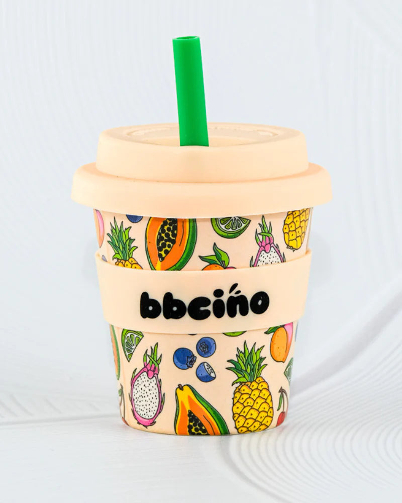 The BBCINO BBcino Reusable Babycino Cup 120ml Troppo (Limited Edition) features a green straw, beige lid and sleeve labeled "bbecíno", plus fruit illustrations—a sustainable bamboo cup that's an eco-friendly choice for drinks.
