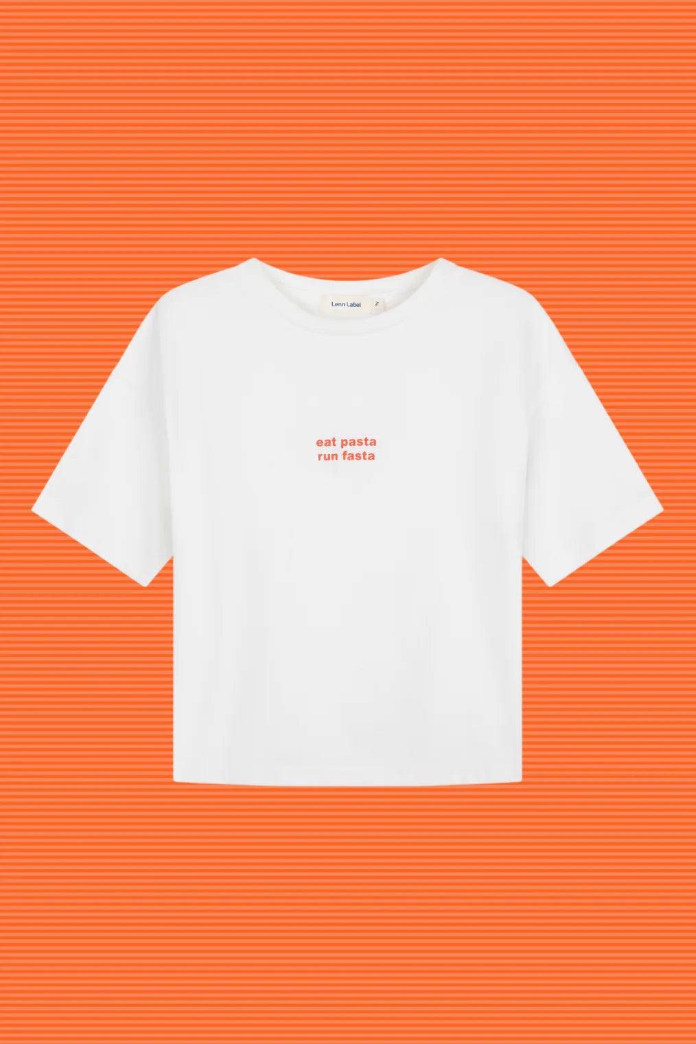 The Lenn Label - Pasta Tee White by LENN LABEL is a white cotton jersey t-shirt with short sleeves and "eat pasta run fasta" in red lowercase letters on the chest, set against an orange background with fine horizontal stripes.
