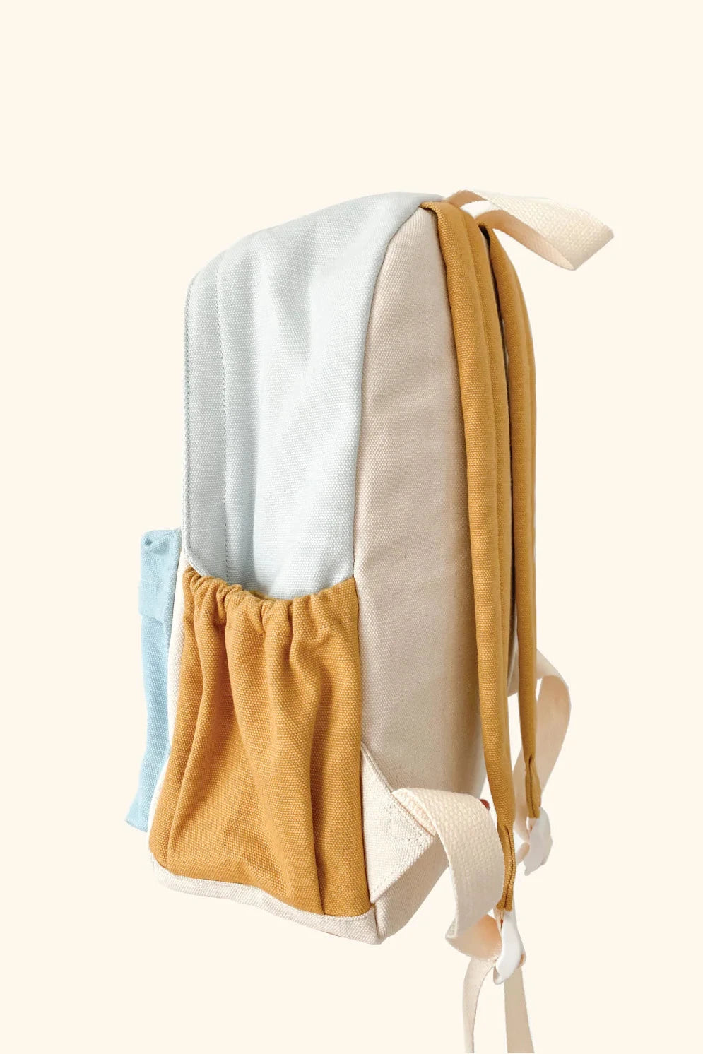 Introducing the Jagger Backpack by ZEPHII, a minimalist kindergarten bag in pastel tones with blue, beige, and mustard-yellow panels. It features a front pocket and adjustable beige straps, making it ideal against a plain light beige background.
