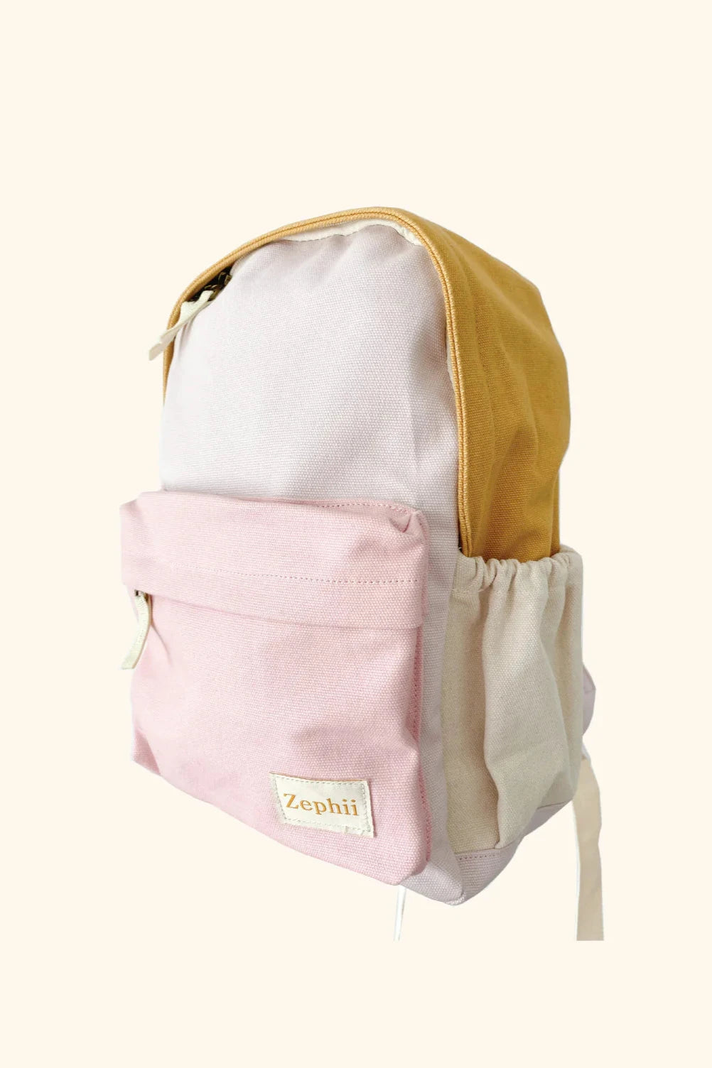 The Poppy Backpack by ZEPHII is a color-blocked kids backpack in mustard yellow, cream, and pastel pink, featuring a front zip pocket, side pockets, and a small “ZEPHII” label.