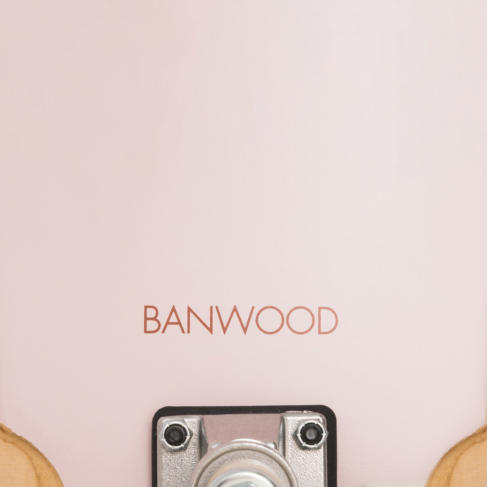 Close-up of the Banwood - Skateboard Pink, made from Canadian Maple, featuring "BANWOOD" on its pink surface. The bottom metal part with a wheel and truck is partially visible against the pale pink backdrop.