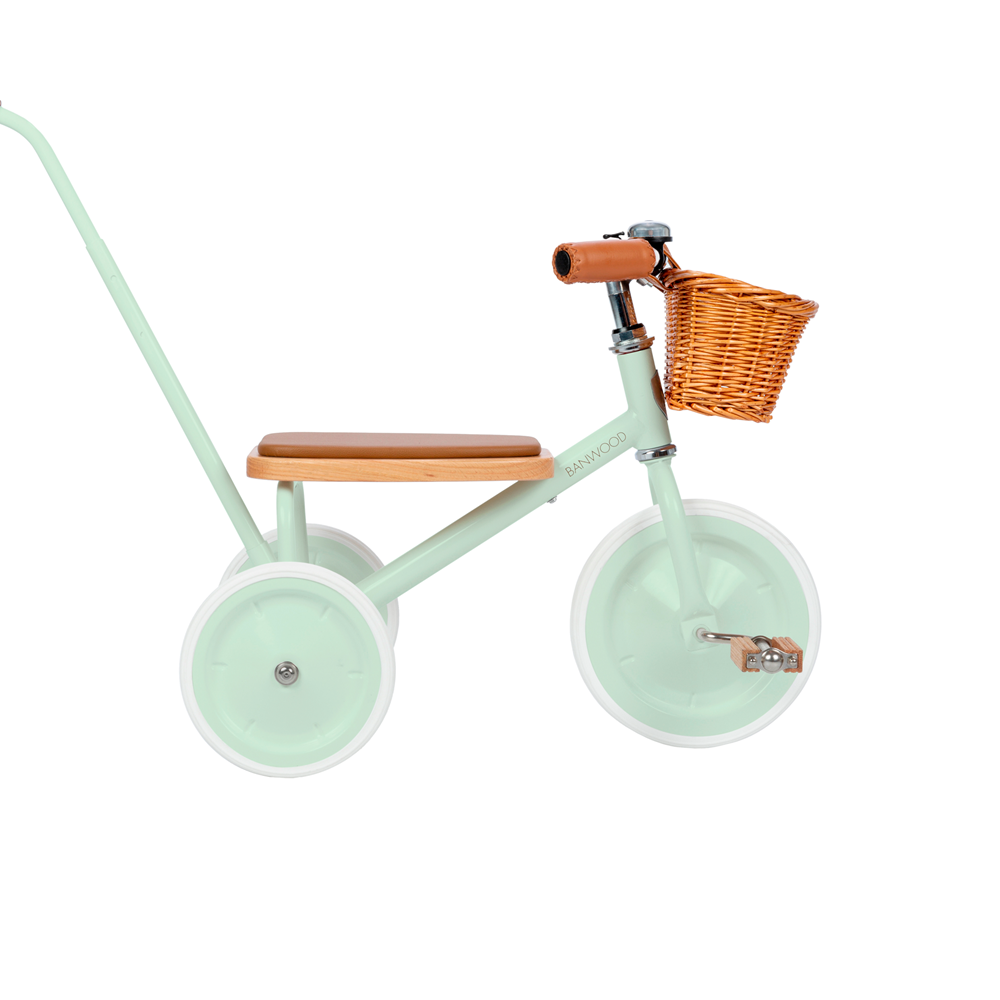 The Banwood - Trike Pale Mint is a delightful kids tricycle featuring a brown wooden seat, handlebars, and wicker basket. It has white tires and a long rear handlebar for easy pushing, blending style with function perfectly for your child's adventures.
