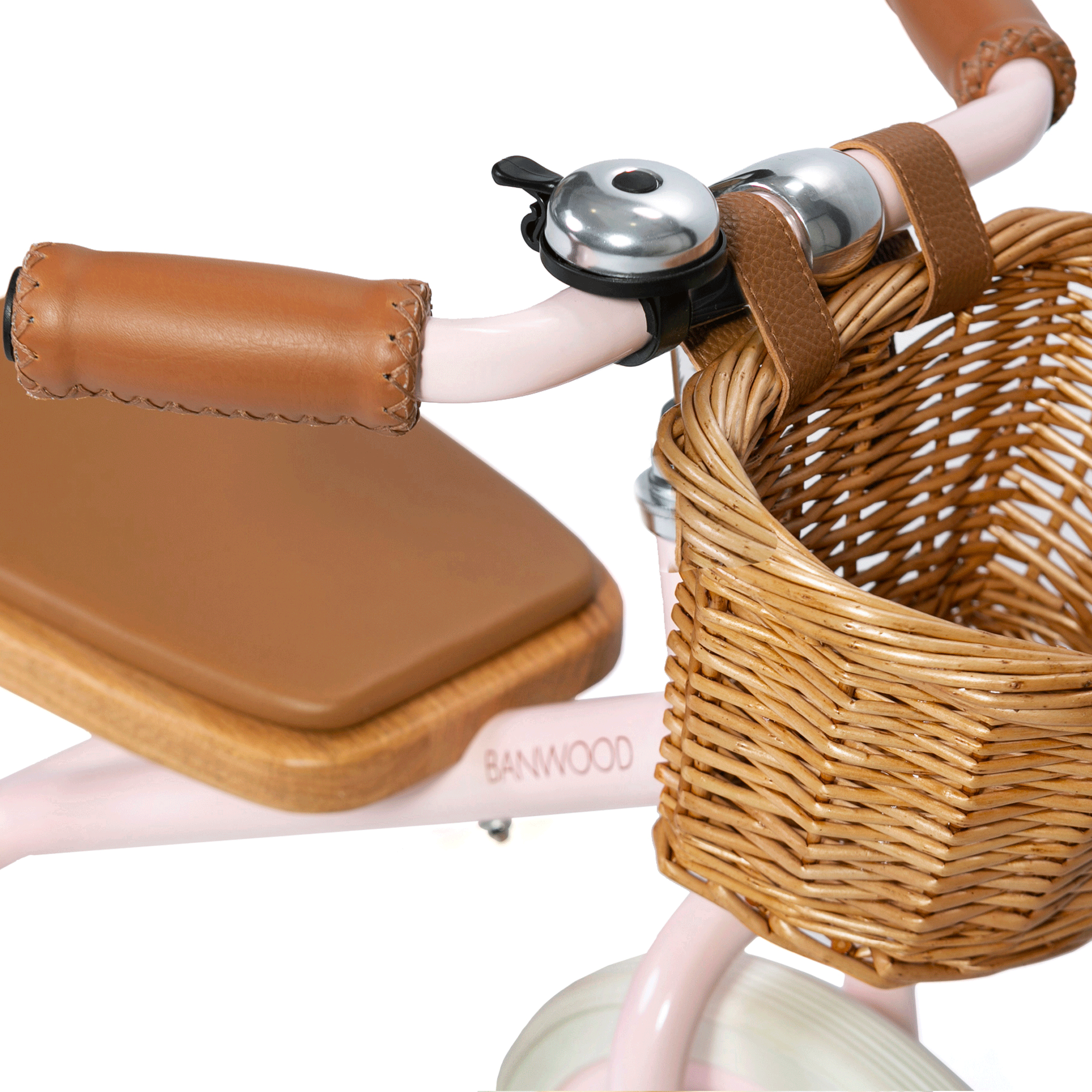 Close-up of the Banwood - Trike Pink, showcasing a woven basket, brown leather-like grips on the handlebars, and a small bell beside the basket. The "BANWOOD" logo is visible on its frame.