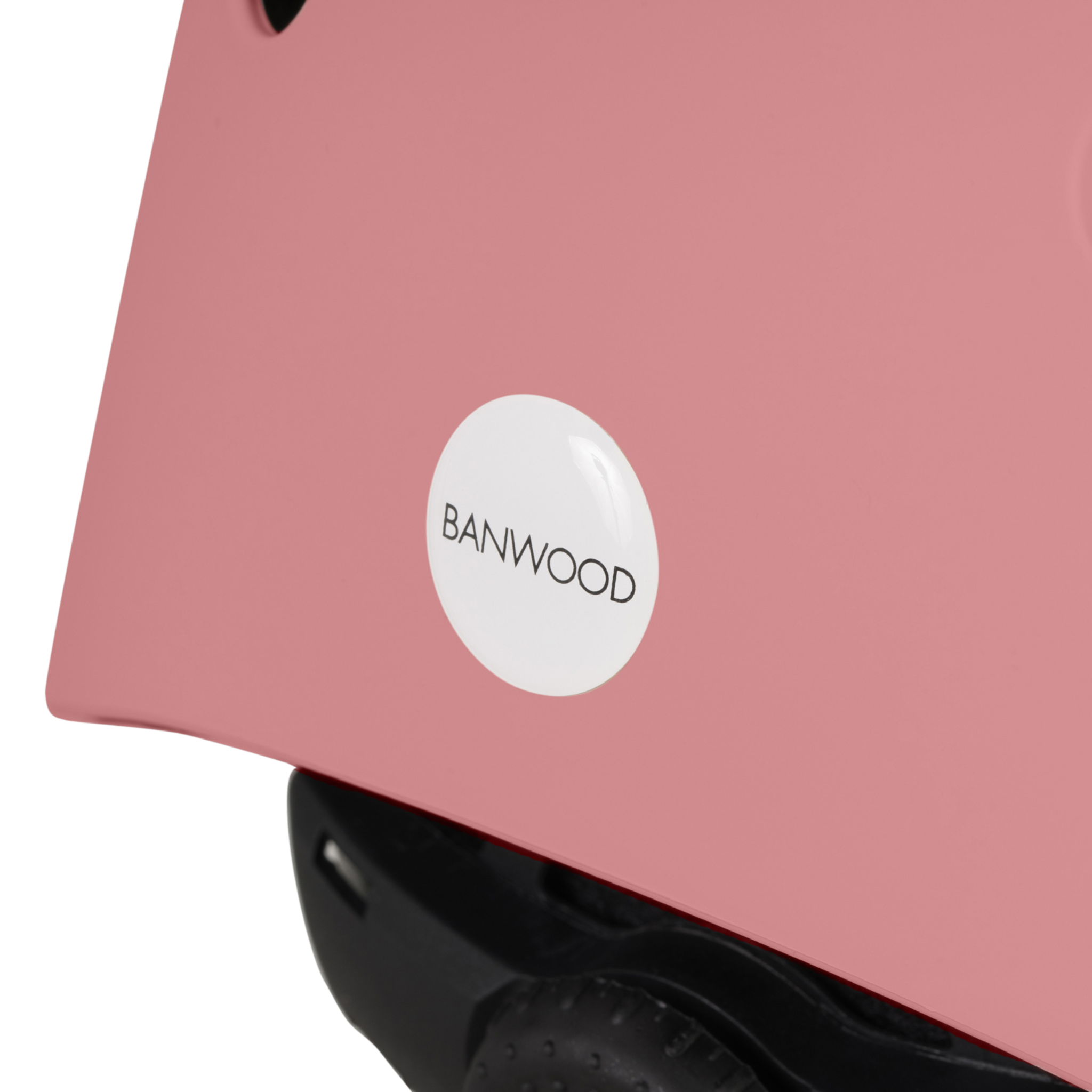 Close-up of a Banwood Eco Helmet in Raspberry, showcasing the BANWOOD logo in black on a white circular emblem. Crafted from recycled materials, it is set against a white background that highlights the logo and part of the helmet's edge.