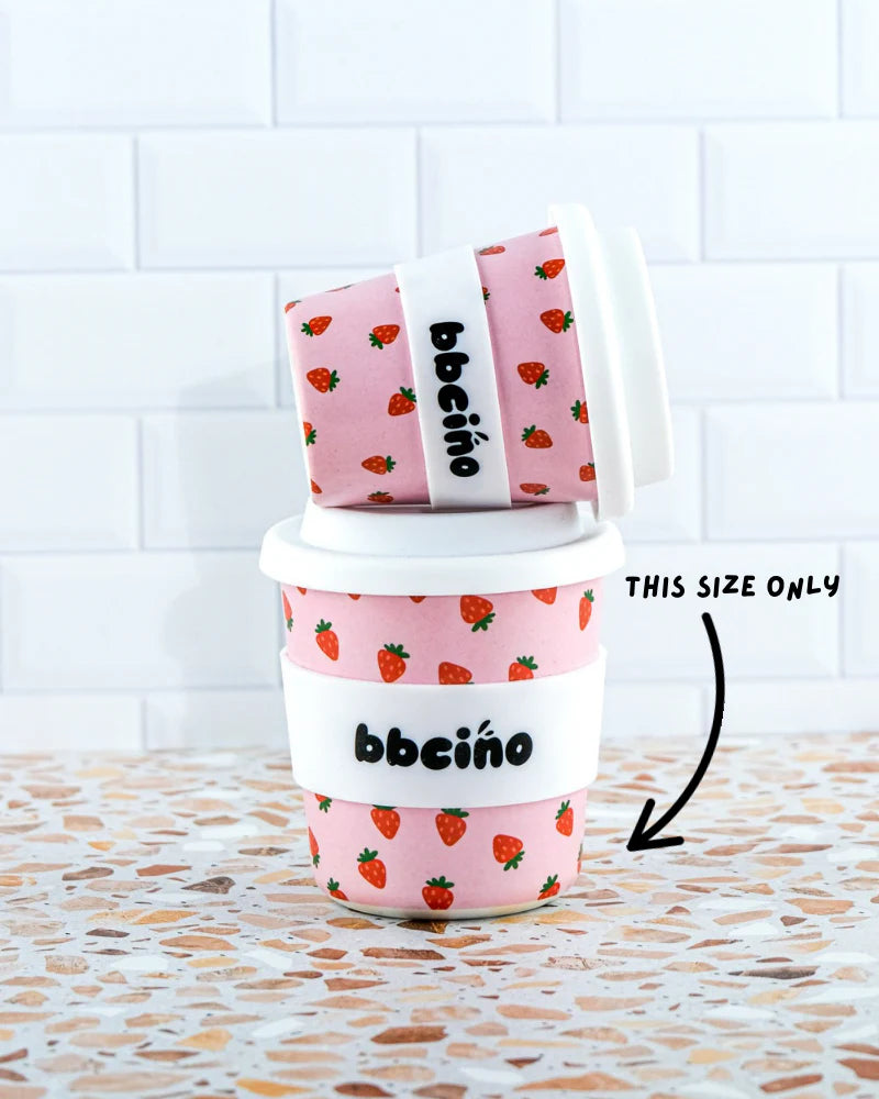 Two BBcino Reusable BambinoCino Cups 240ml Berry BB by BBCINO, featuring a strawberry pattern and white lids, sit on terrazzo. Made from sustainably farmed bamboo, these eco-friendly cups are ideal for little ones.