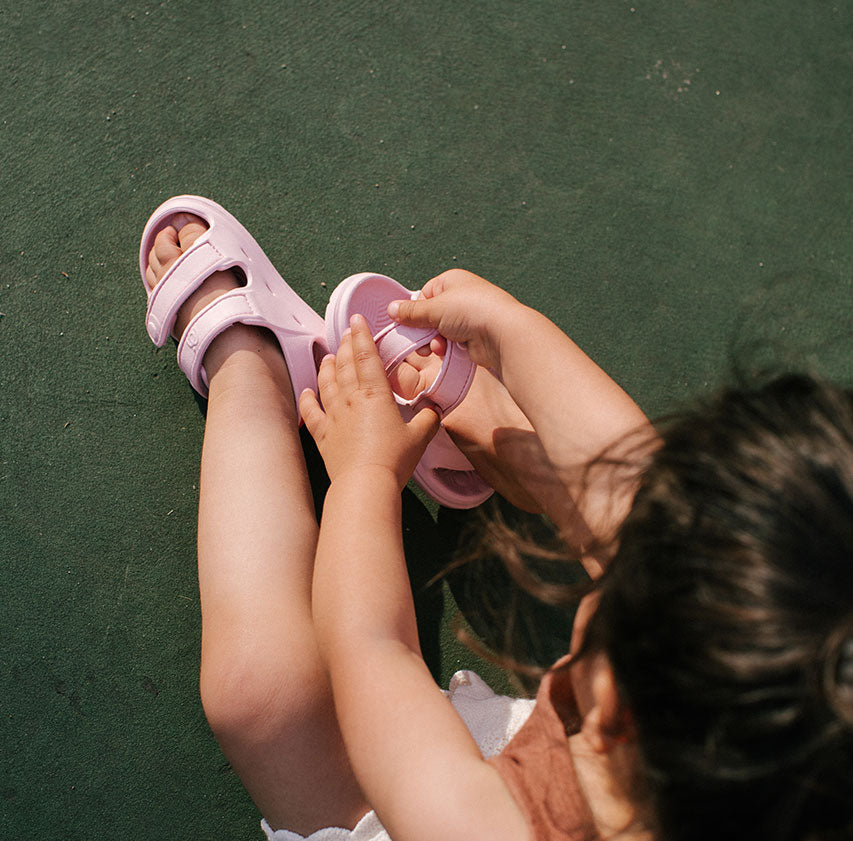 Toddler putting on Simples WonderSkips sandals in Petal Pink