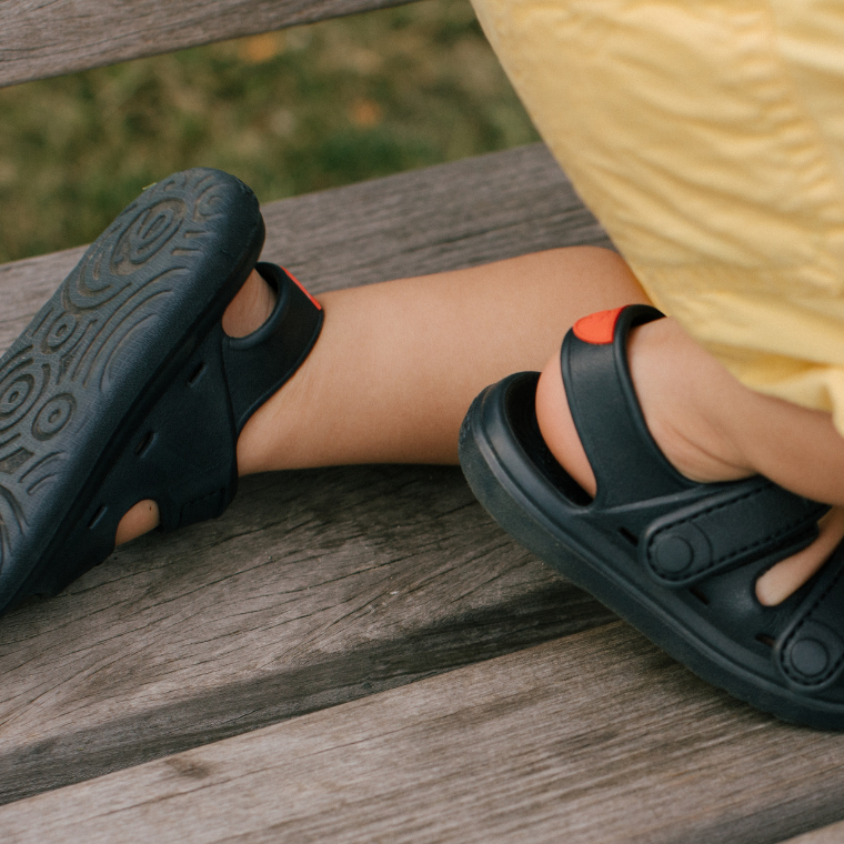 Child sitting on a bench wearing Simples WonderSkips sandals in Bondi Blue