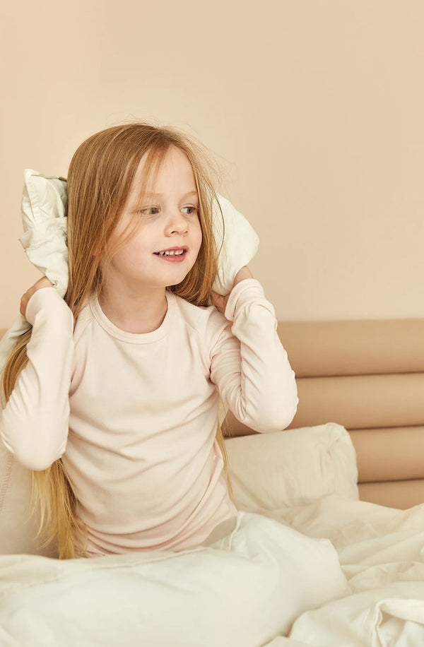 Girl sitting on bed with pillow behind her head wearing sleep set in shell