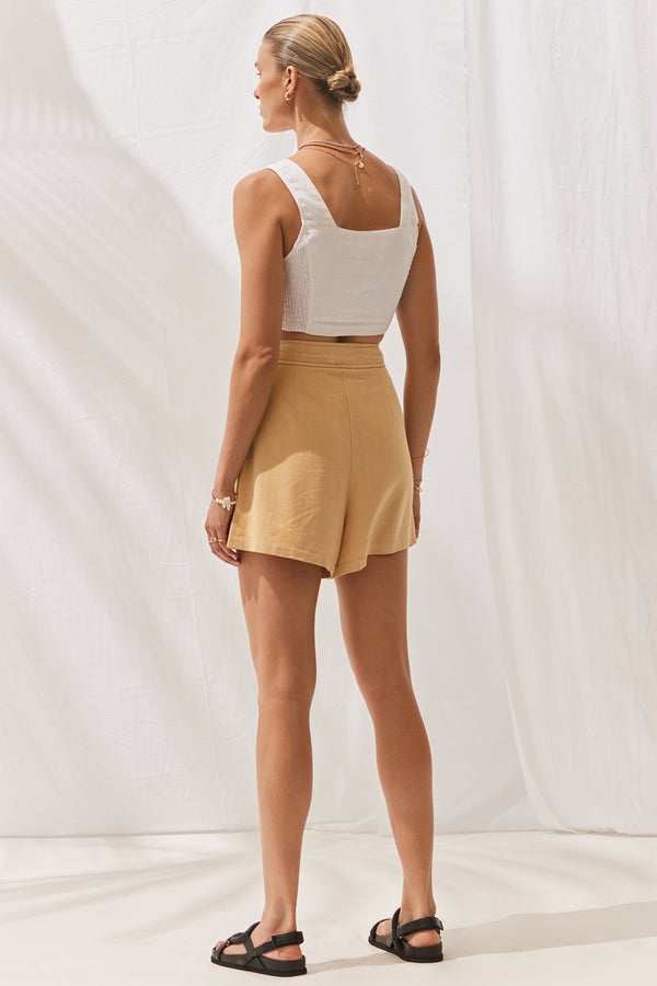 Woman wearing Kiki Shorts in Saffron with cropped white top. Full length, rear view.