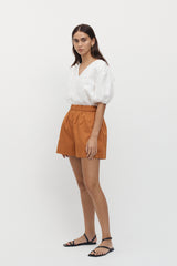 Side view of woman wearing Giverny Puff Sleeve Top in white with burnt orange shorts.