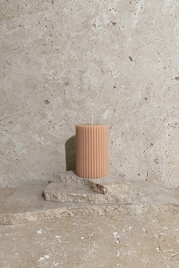 Ribbed pillar candle peach on stack of travertine