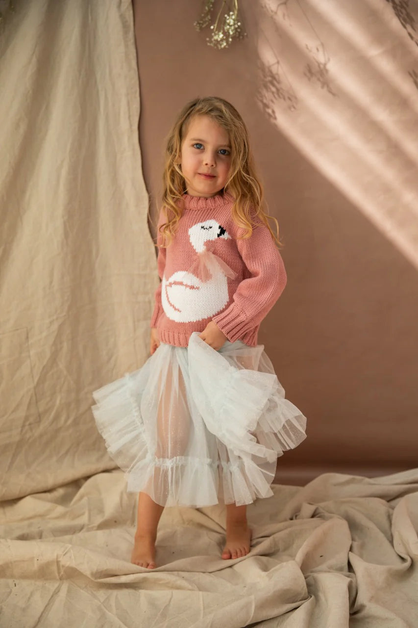 A young girl wearing the carrie iced lake tutu and a coral knitted sweater against a brown draped background.