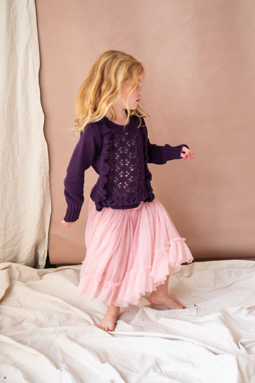 A young girl twirling in the carrie tutu in the pink lady apple colour. She is standing on a cream drape against a brown wall.