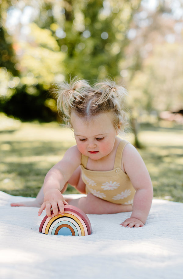 Baby playing with rainbow stacker on a playmat in the garden