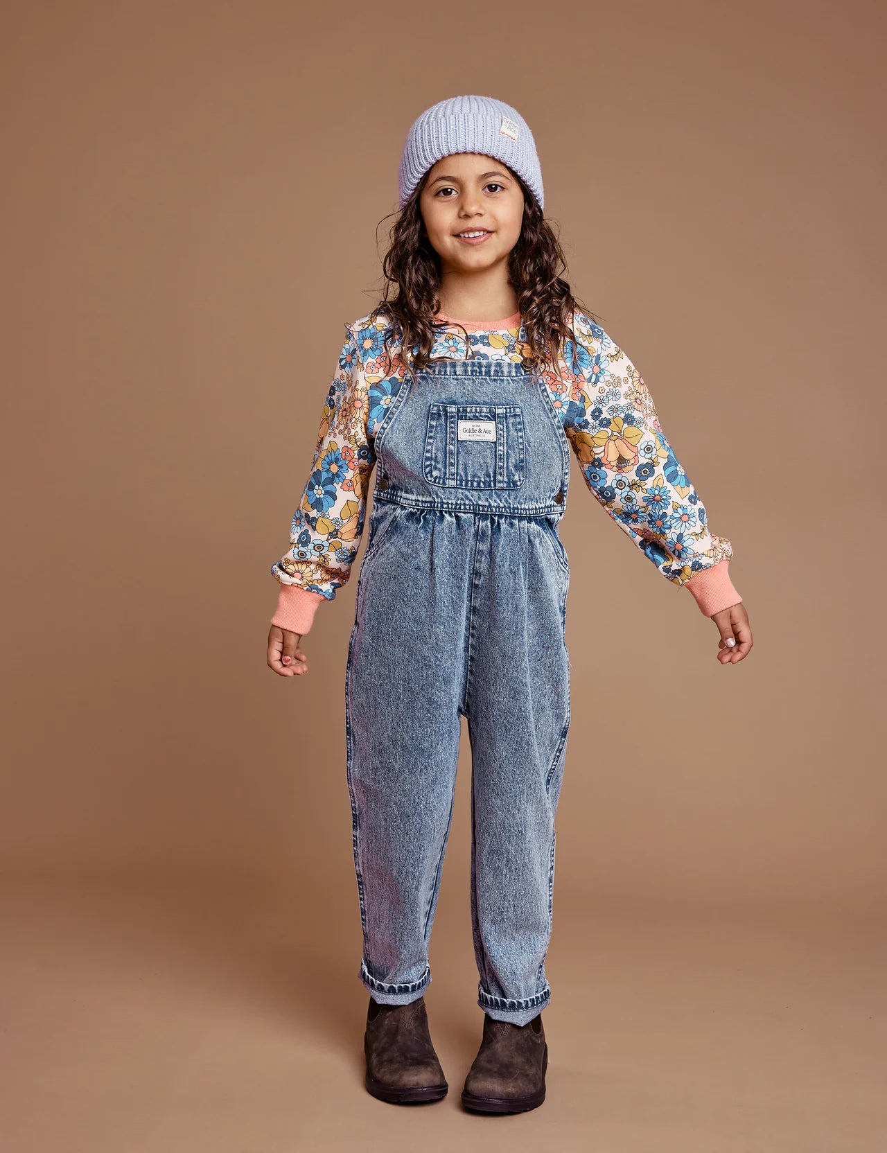 A young girl wearing overalls and boots with the GOLDIE + ACE  Wool Beanie in lilac.