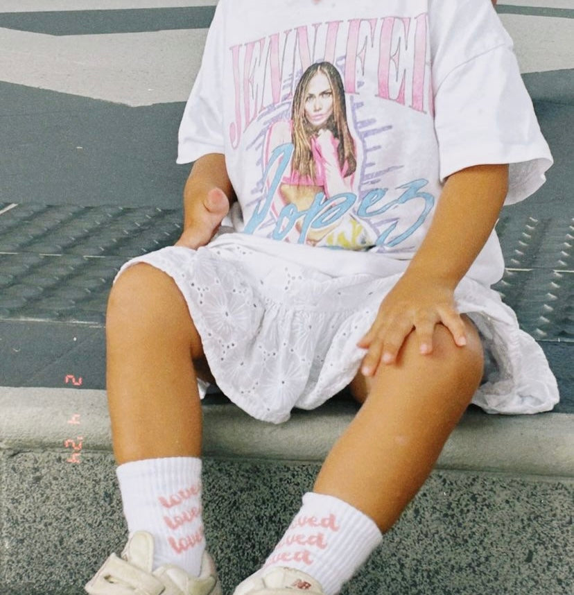 A young girl wearing the another love sock with sneakers and a white skirt and t shirt.