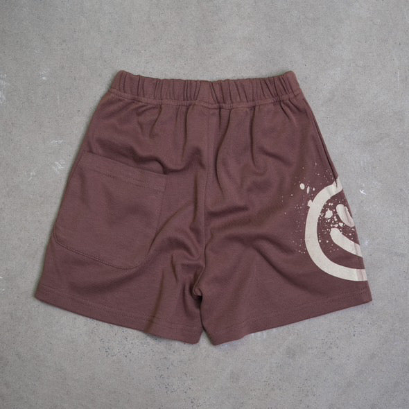 Acid Dye Shorts Brown by FRANCO'S DAD, size 1: Stretch cotton with an elastic waistband, single back pocket on the left. The right side sports a white circular paint-splatter design. Perfect for lounging, displayed on a gray textured surface.