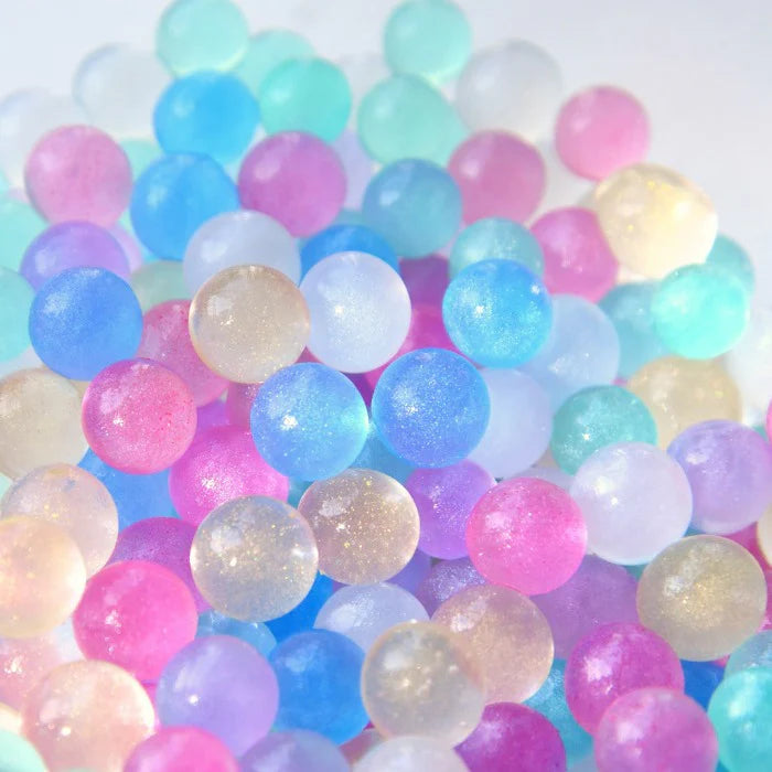 The Unicorn Bubbles Pastel Biodegradable Water Beads by NO NASTIES shimmer with vibrant hues of pink, blue, purple, green, and clear, creating a captivating sensory play experience that boosts fine motor skills.