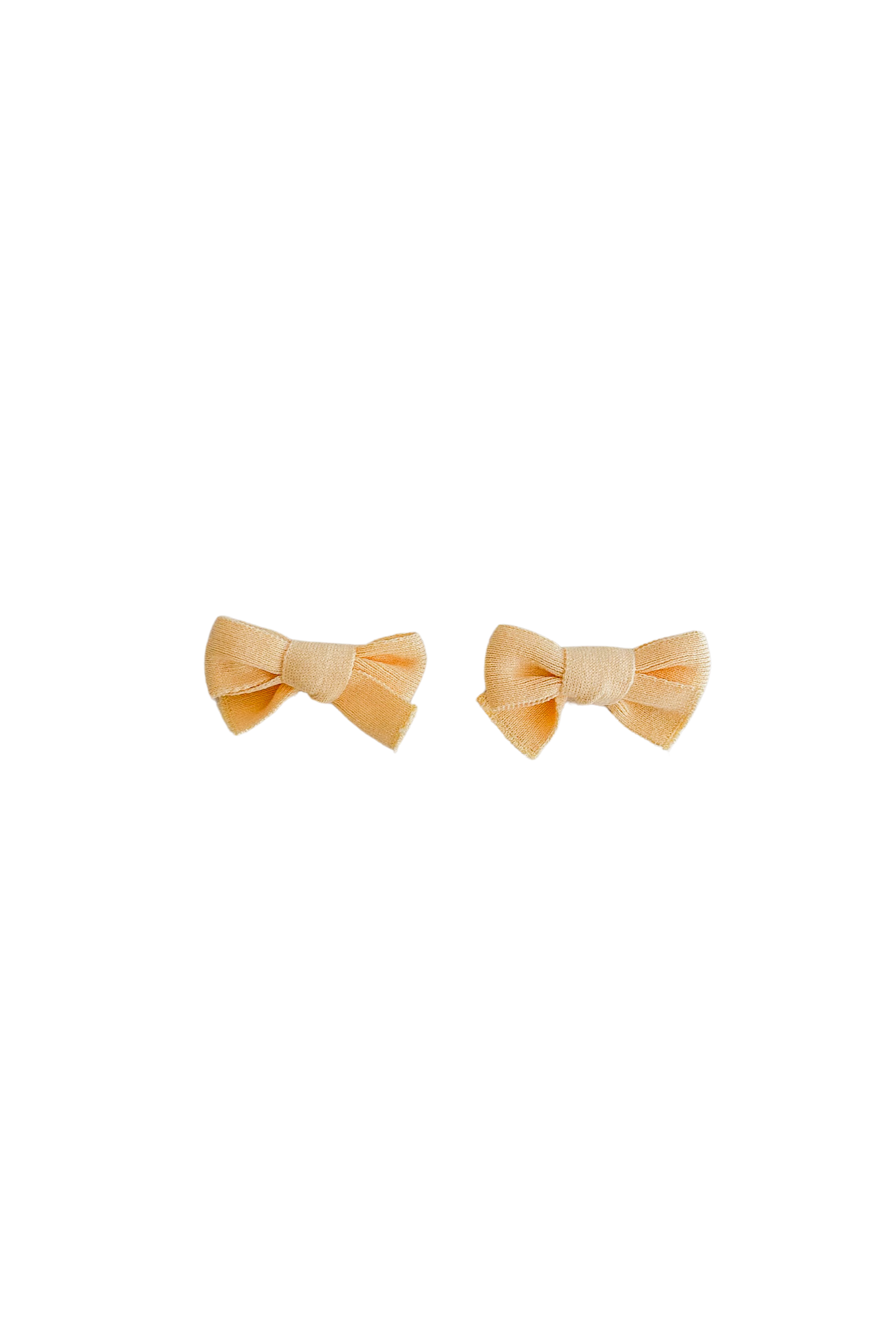 The "Bows Butter" by ZIGGY LOU features two small, butter-colored fabric bows crafted from 100% cotton, set against a solid black background. Each knitted bow hair clip is meticulously tied to showcase symmetrical loops and tails.