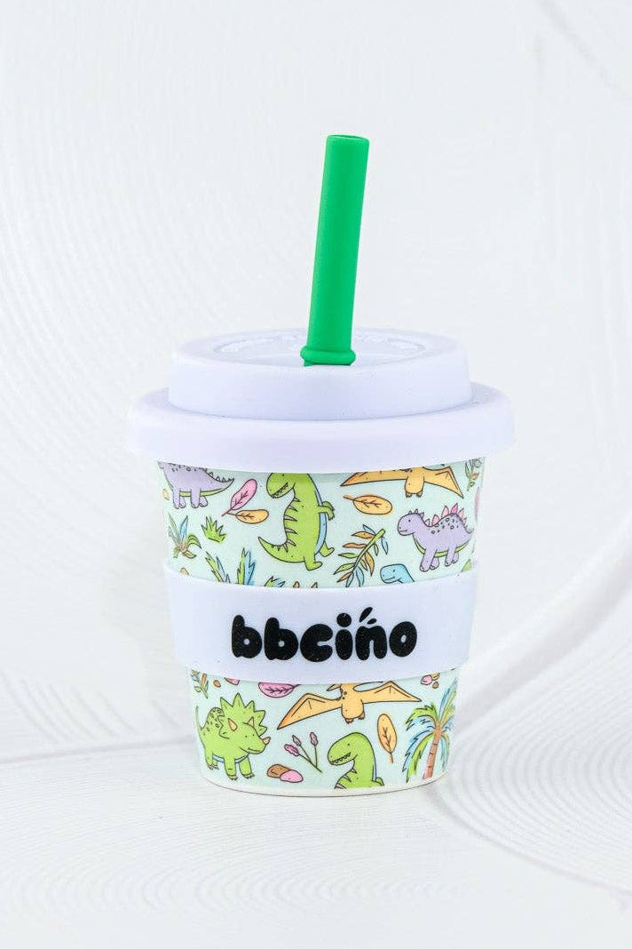 The BBcino Reusable Babycino Cup 120ml Sip-a-saurus features eco-friendly bamboo, a green straw, white lid, and playful dinosaur designs—perfect for fun-loving kids who want a colorful, sustainable cup. Set against a white textured background.
