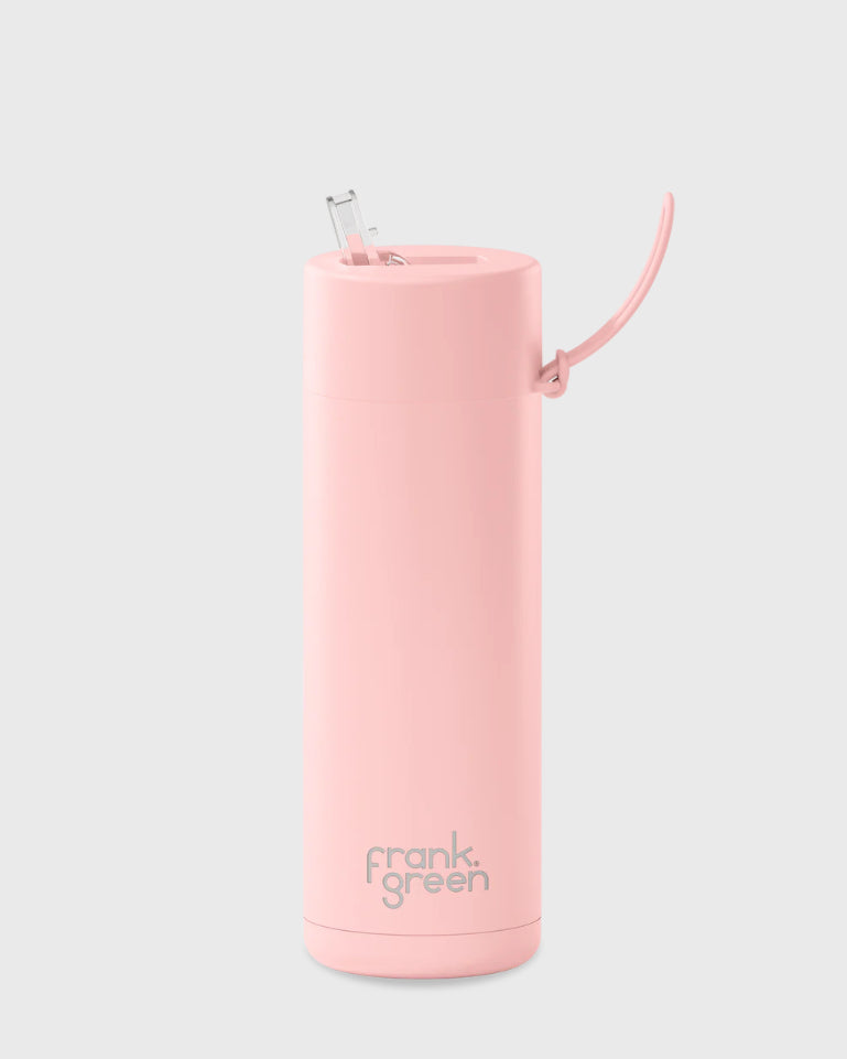 The Frank Green Ceramic Reusable Bottle 595ml 20oz Straw Lid in Blushed is a tall, pink travel mug with the brand name "FRANK GREEN" printed in gray near the base. Crafted from stainless steel, it boasts triple-wall vacuum insulation. The slender cylindrical design includes a raised spout with a clear straw and a small handle attached to the lid. The background is light gray.