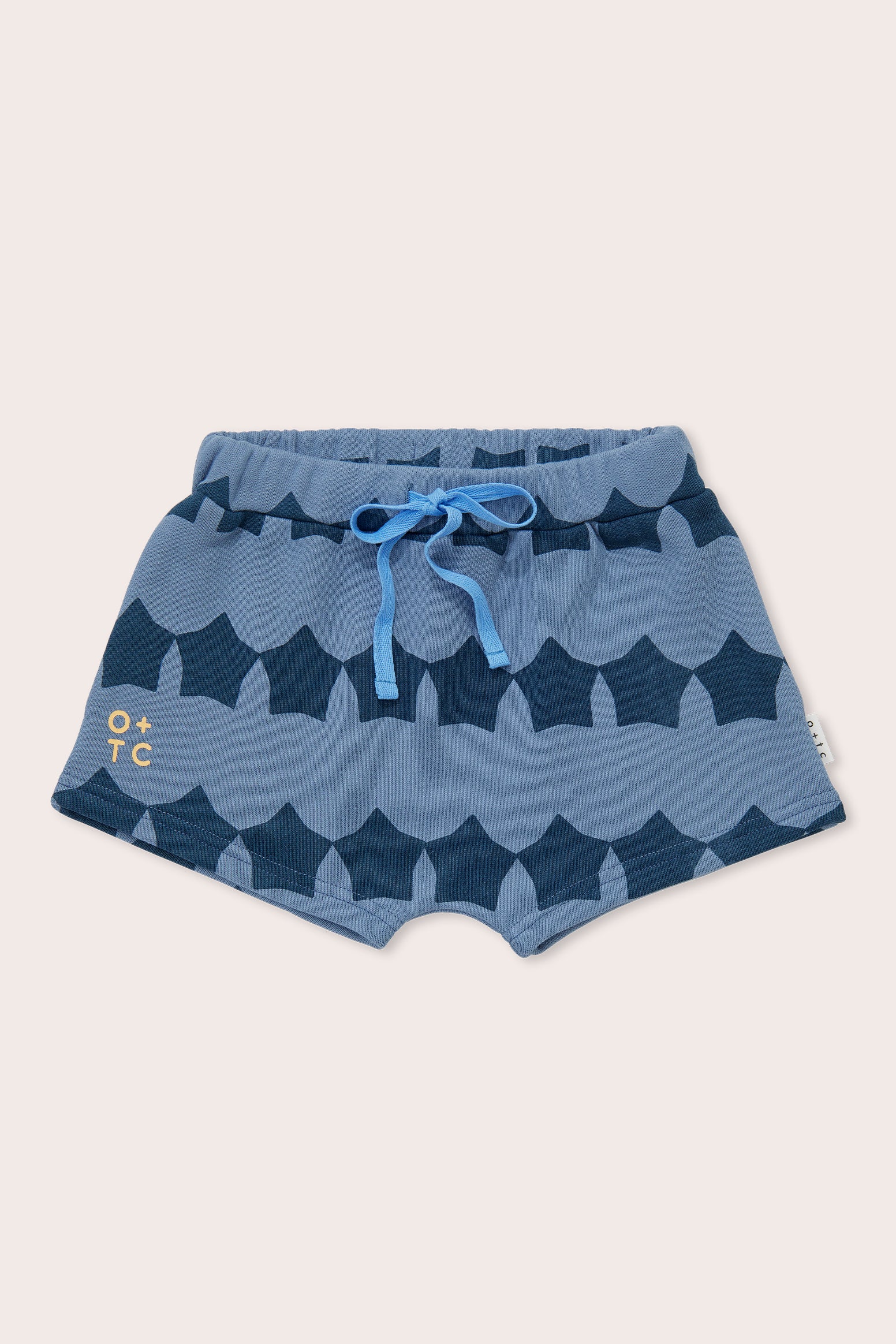 Midnight Supernova Shorties by OLIVE + THE CAPTAIN are blue toddler shorts featuring a wave pattern in navy and lighter blue. Made from 100% cotton, they have an elastic waistband, a light blue drawstring, and "O+TC" printed in yellow near the left hem, reflecting stylish design from the Olive and the Captain collection.