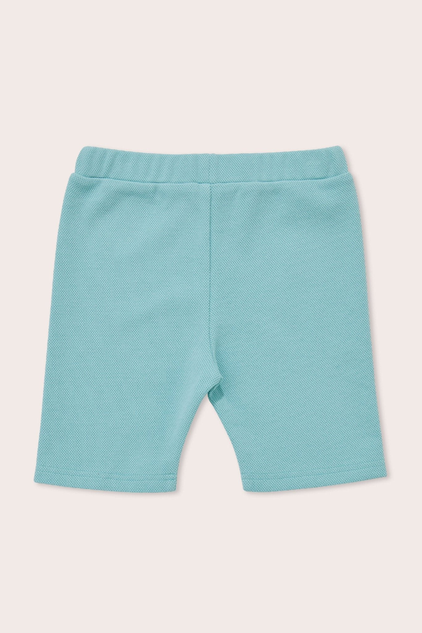 A pair of Aqua Sky Bike Shorts by OLIVE + THE CAPTAIN is displayed against a plain beige background. Made from a premium, textured fabric, these light blue toddler bike shorts feature an elastic waistband and are designed for comfort and flexibility.