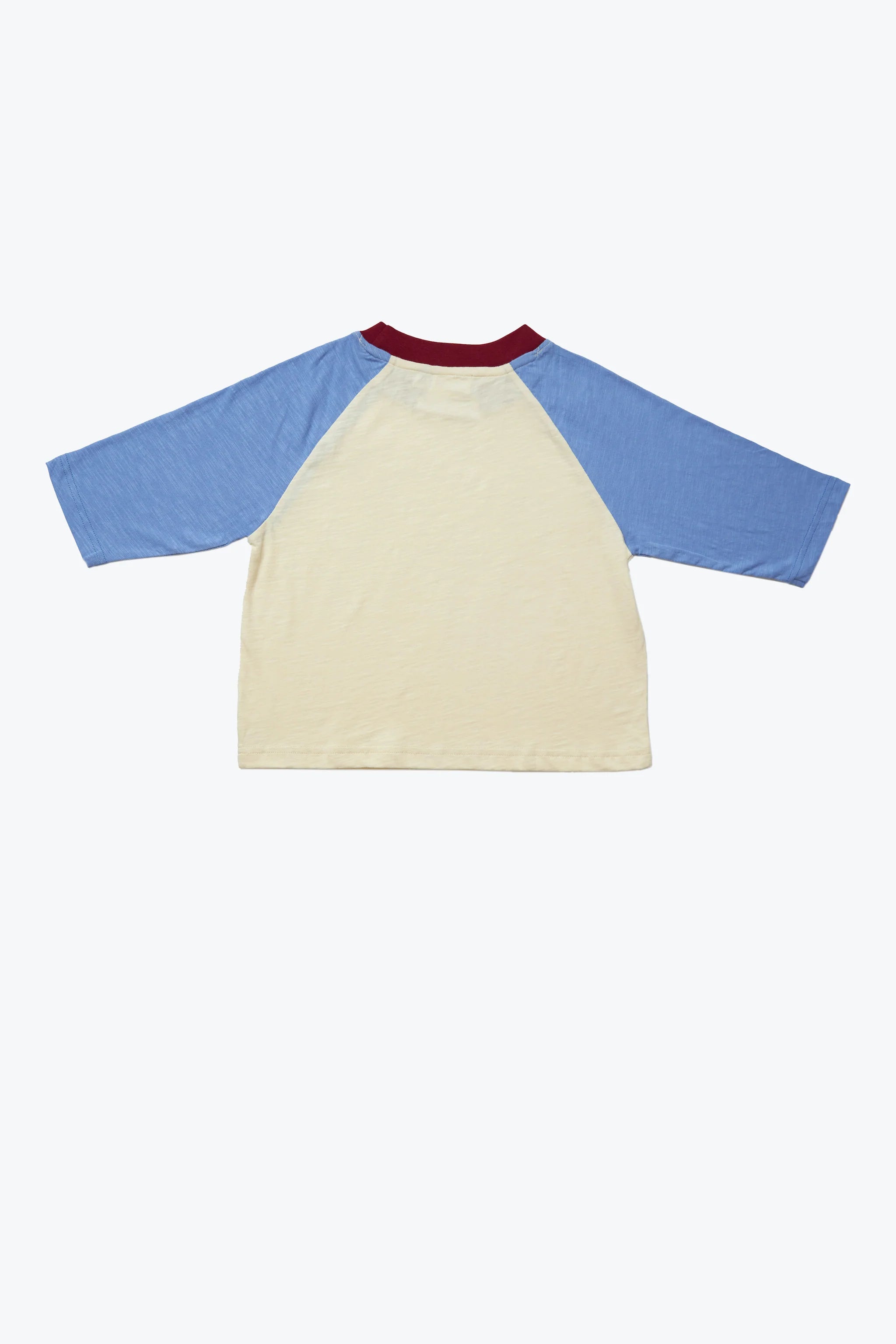 The Weekend Raglan Long Sleeve Tee by KOKOMO is displayed from the back, showcasing its child-sized design with a red collar, off-white body, and light blue three-quarter length sleeves. Crafted from organic cotton, this t-shirt is neatly presented against a plain white backdrop.