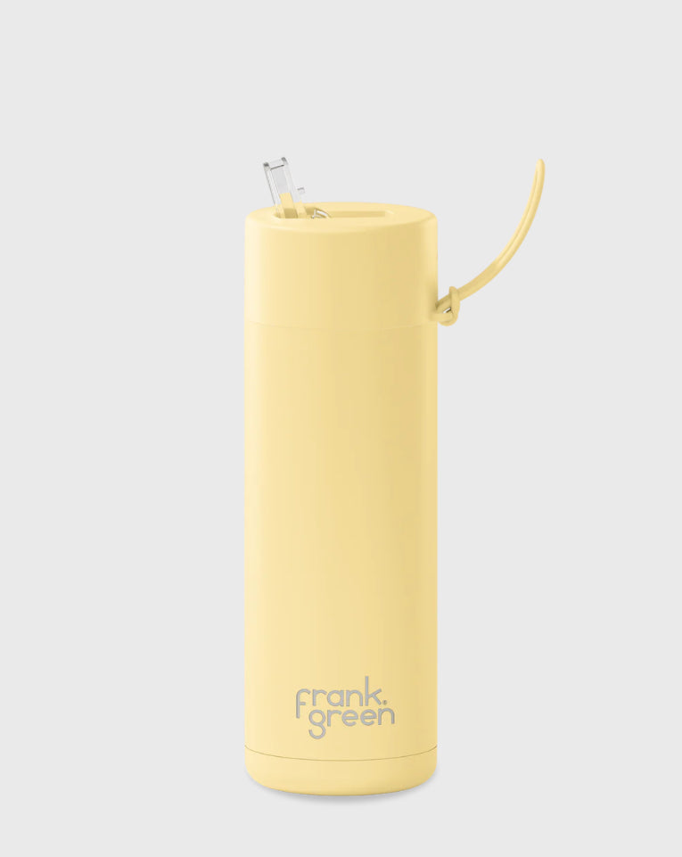 A tall, cylindrical Frank Green Ceramic Reusable Bottle with a 595ml (20oz) capacity, featuring a Buttermilk yellow color and "FRANK GREEN" written on the bottom. Made from durable stainless steel and vacuum insulated, it keeps your drinks at the perfect temperature. The bottle comes with a flip-up straw lid and handle. The background is plain grey.