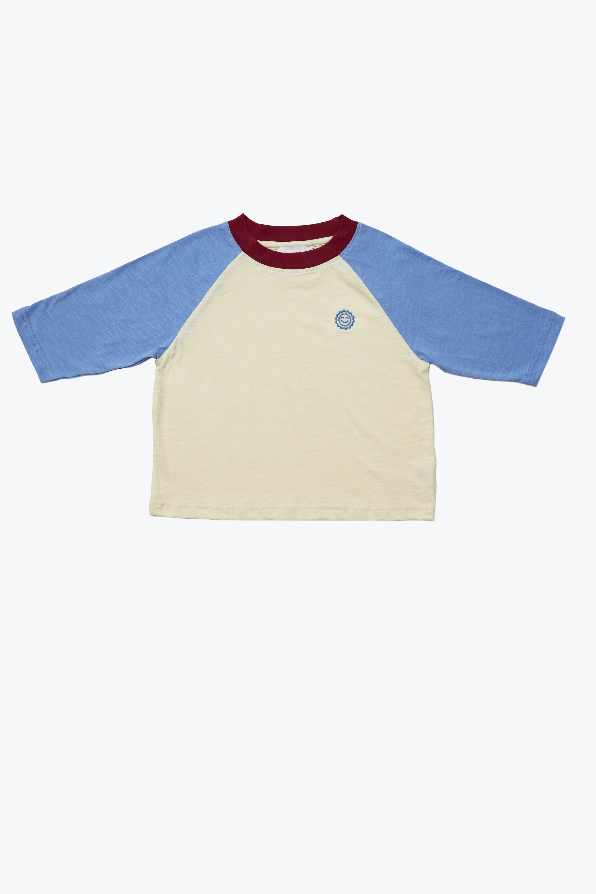 The Weekend Raglan Long Sleeve Tee from KOKOMO offers a relaxed fit with light blue raglan sleeves, a cream torso, and a red collar, all made from organic cotton. It is adorned with a small circular logo on the left chest.