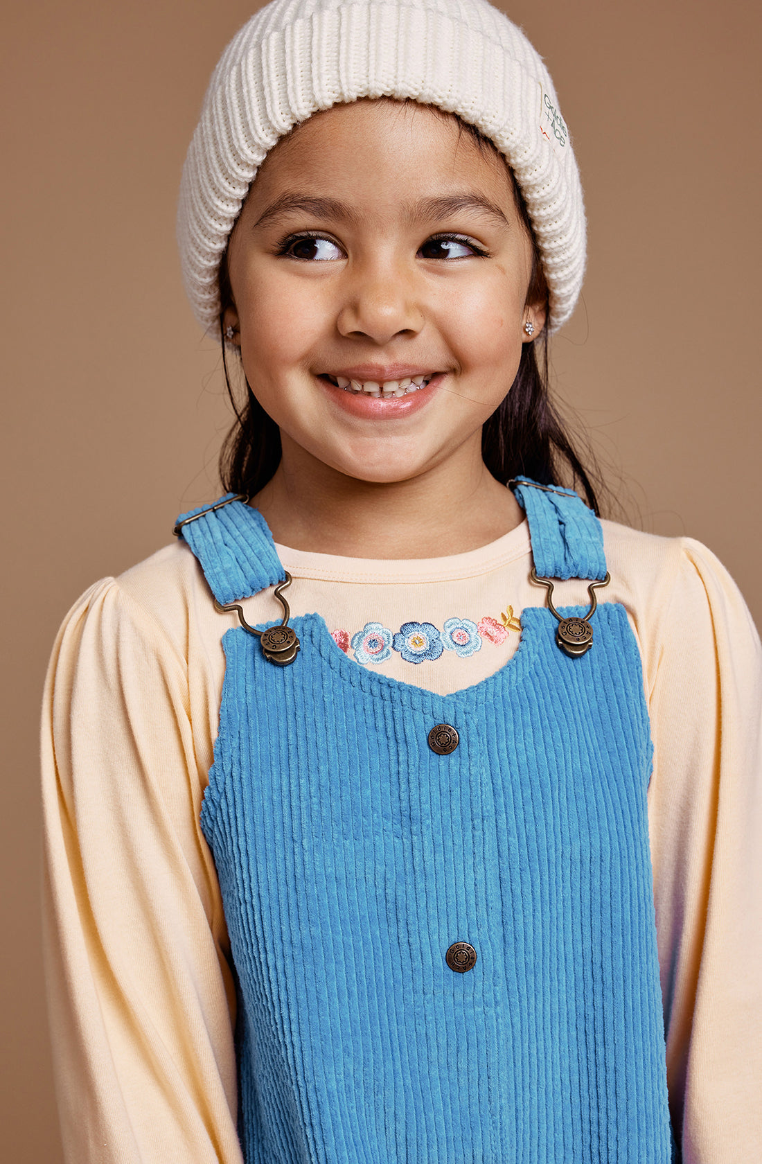 A young girl wearing overalls and a yellow top wearing the GOLDIE + ACE  Wool Beanie in marshmellow