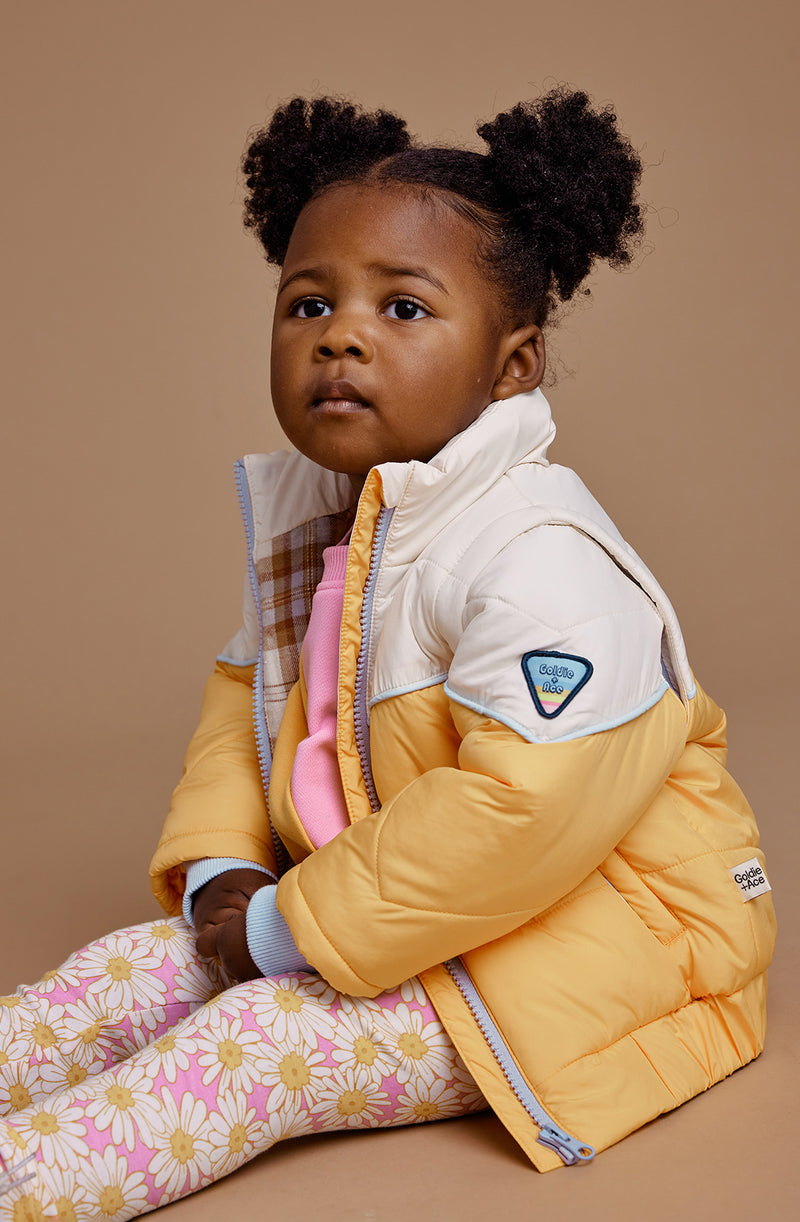 A young girl sitting down wearing the GOLDIE + ACE  Stevie Vintage Parka Golden/Marshmallow.