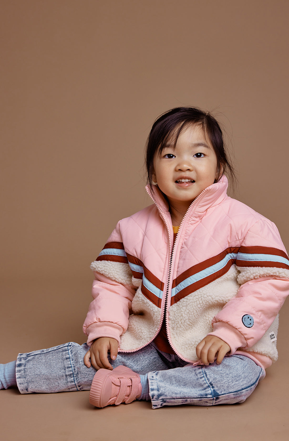 A young girl sitting down wearing the kobe shearling jacket in tulip pink.