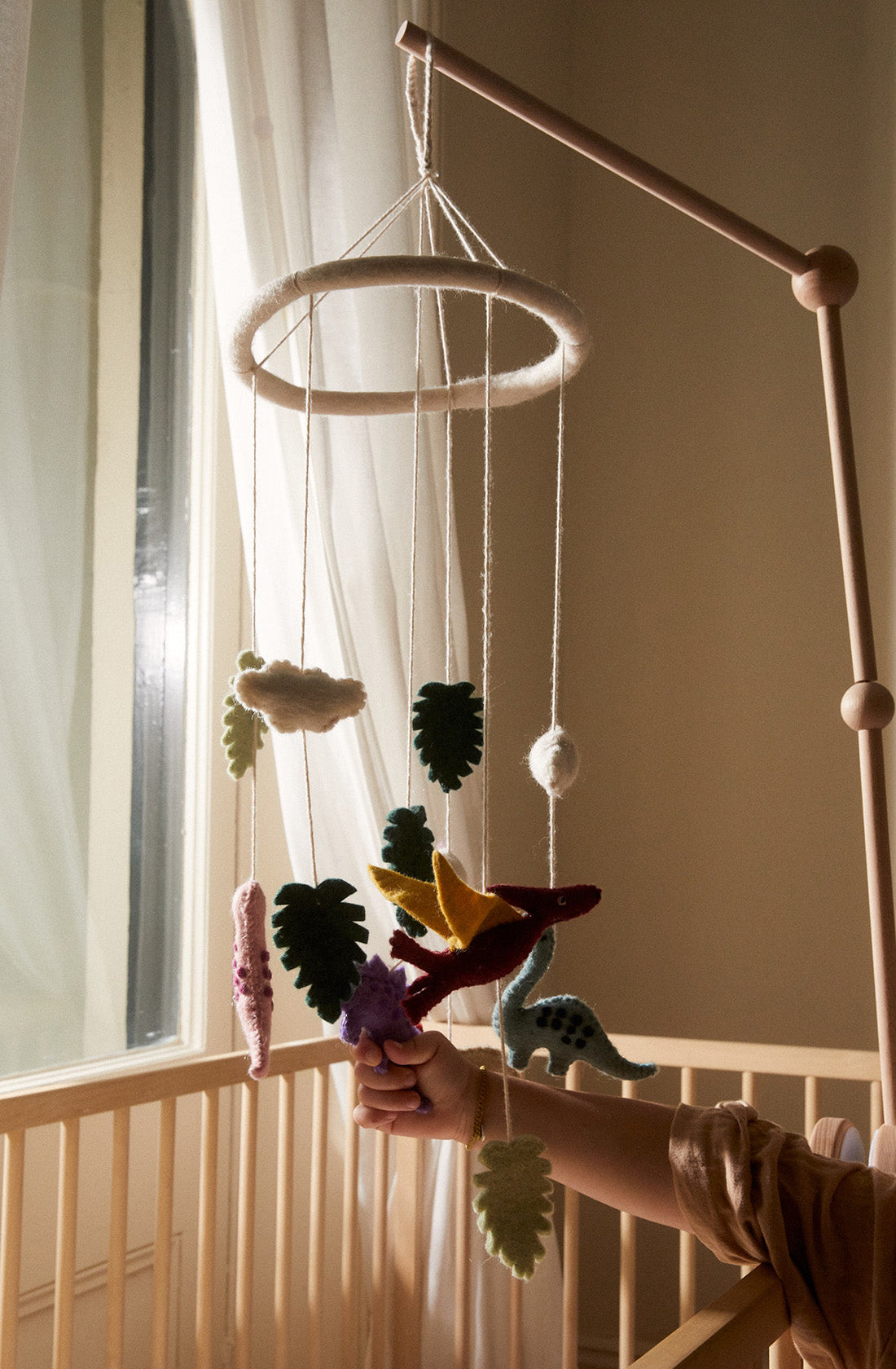 the PHILÉ baby mobile hanging above a cot with a hand grabbing the hanging dinosaurs.