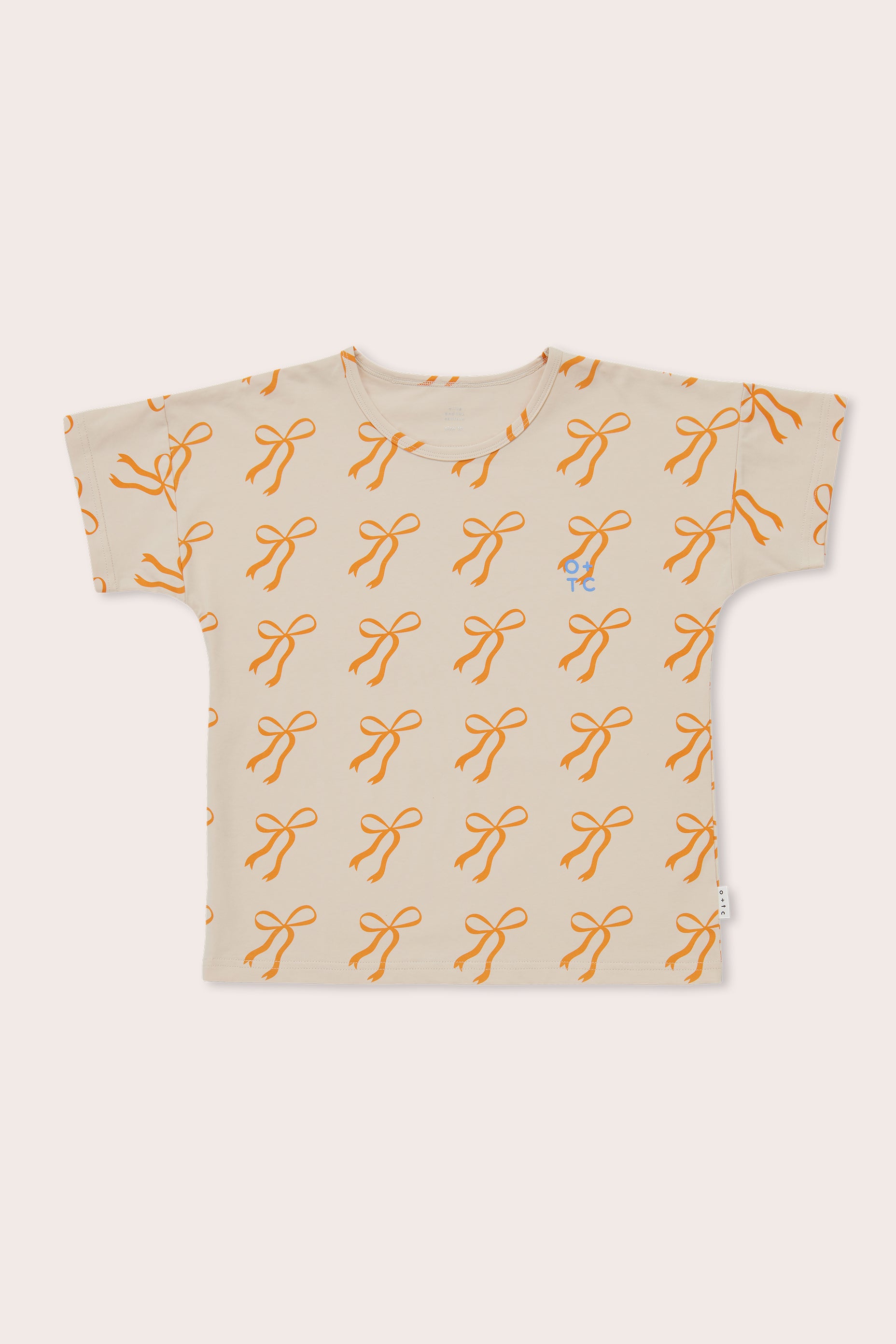 The Cream Bows Relaxed Fit Tee by OLIVE + THE CAPTAIN is a beige children's t-shirt made from a premium cotton blend, featuring a playful all-over print of orange bow knots. It has short sleeves, a round neckline, and a boxy fit, with an embroidered small character wearing glasses on the left chest area.