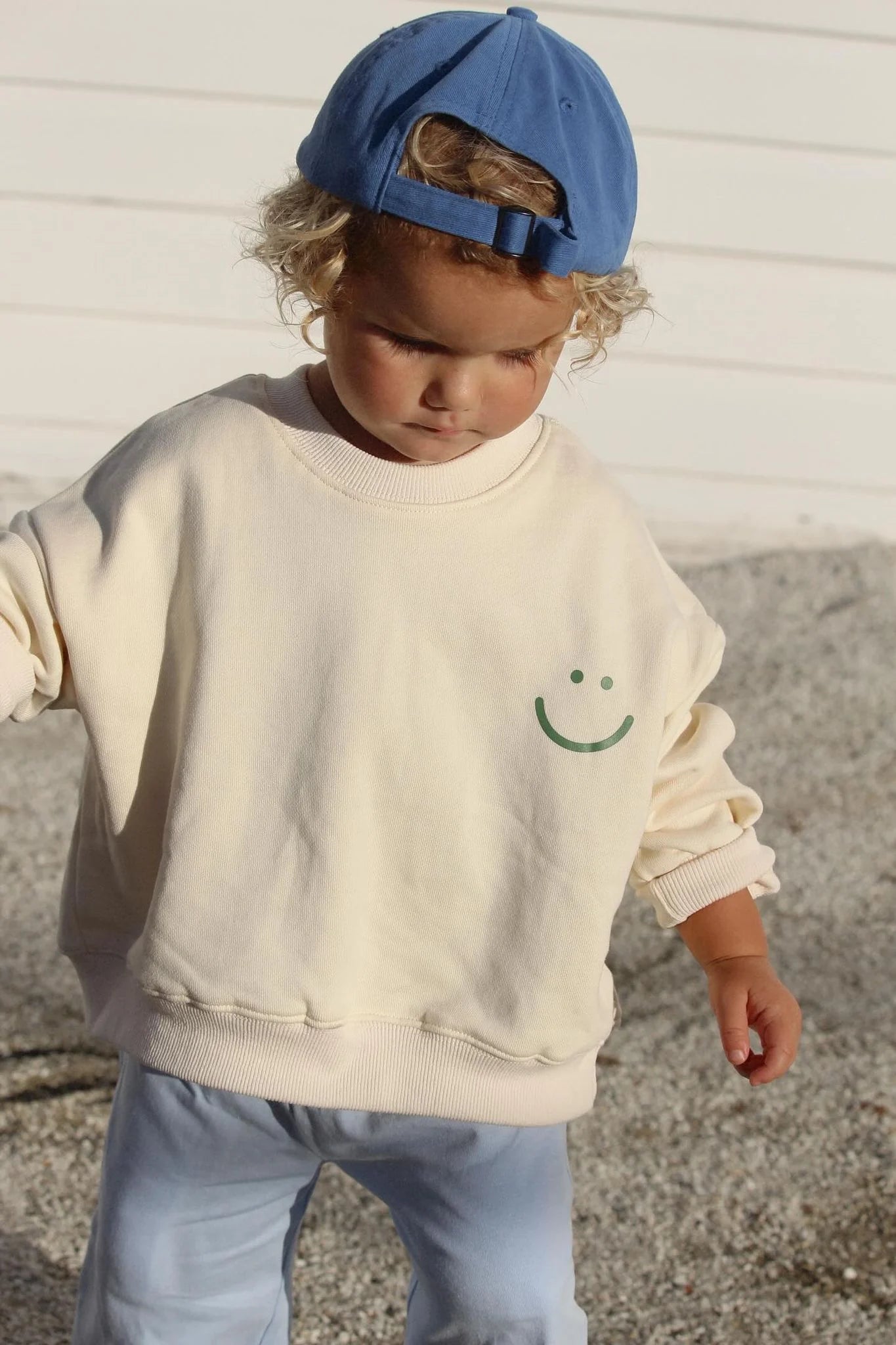 Young boy wearing the wave of life pullover in creme and a blue hat and pants.