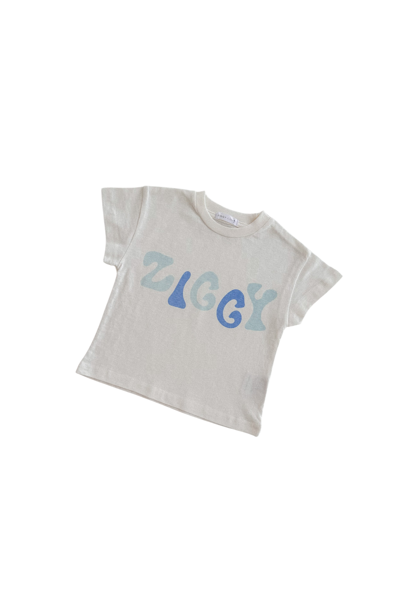 The Print Tee Zen from ZIGGY LOU's Zen Summer Collection showcases an oversized fit with short sleeves and displays the brand name "ZIGGY" in bold, stylized blue and light blue letters. Ethically made, it is photographed laid flat against a striking black background.